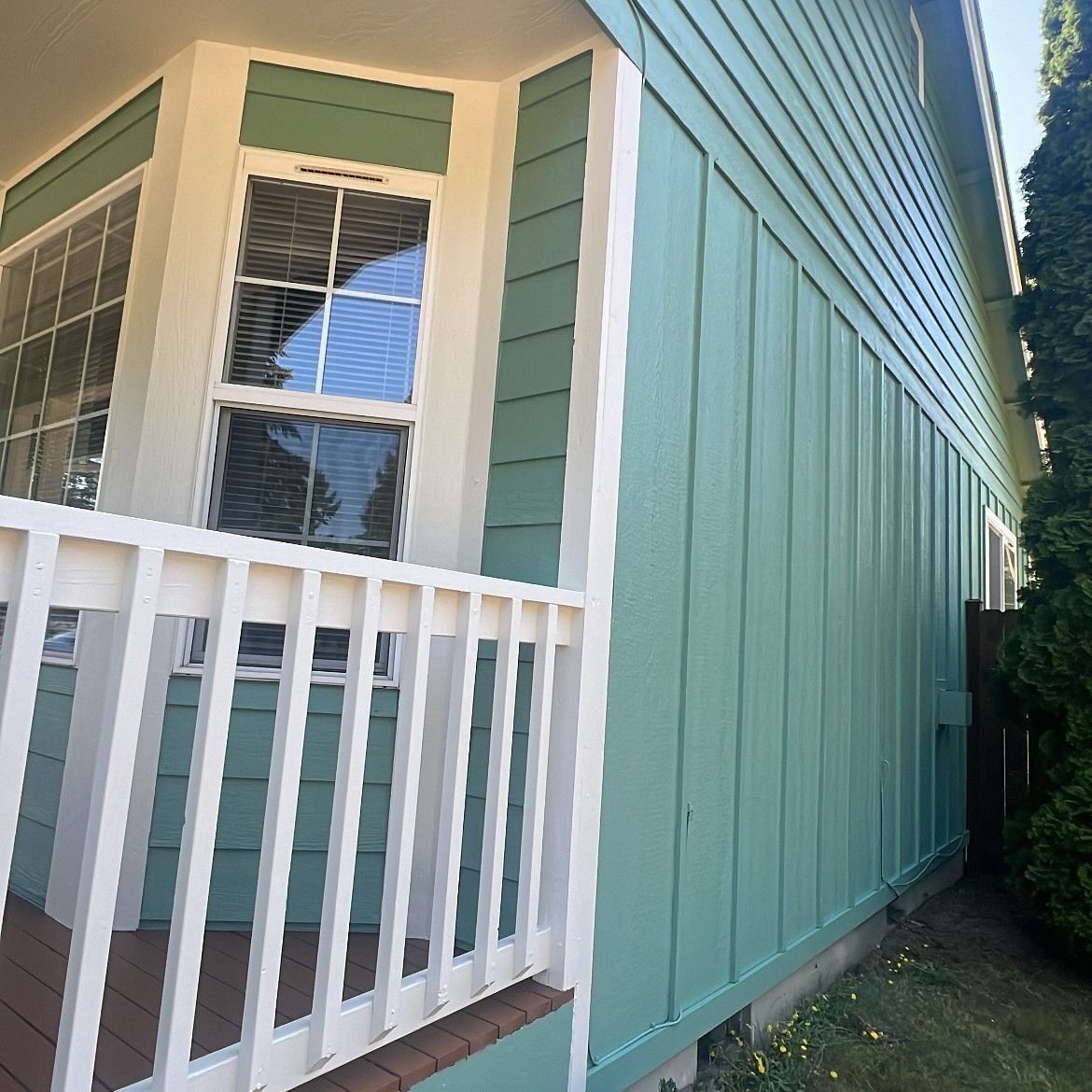 A side view of a house with green siding and white trim, with a porch and windows.