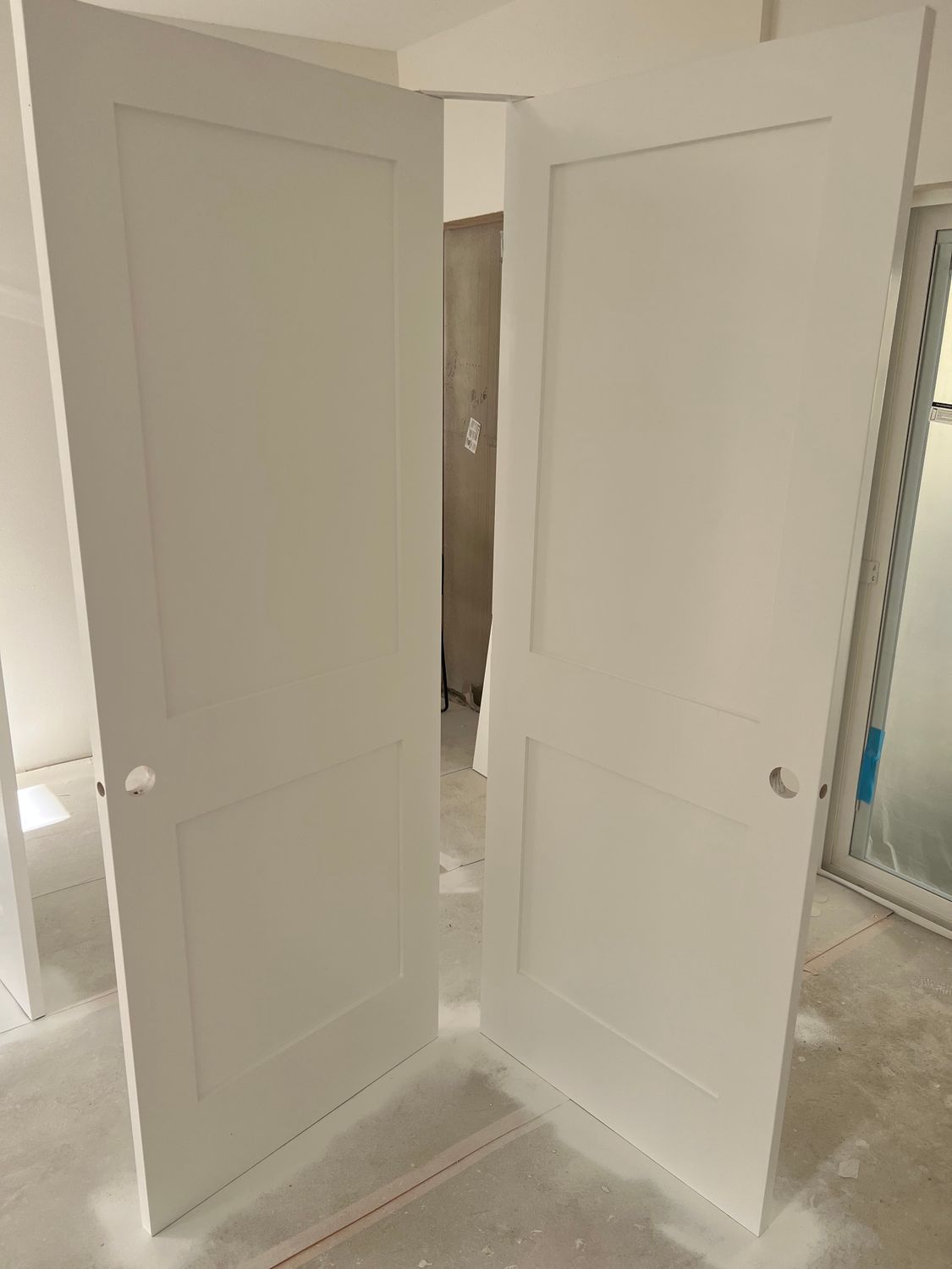 Two white, paneled doors in an unfinished room, slightly ajar.