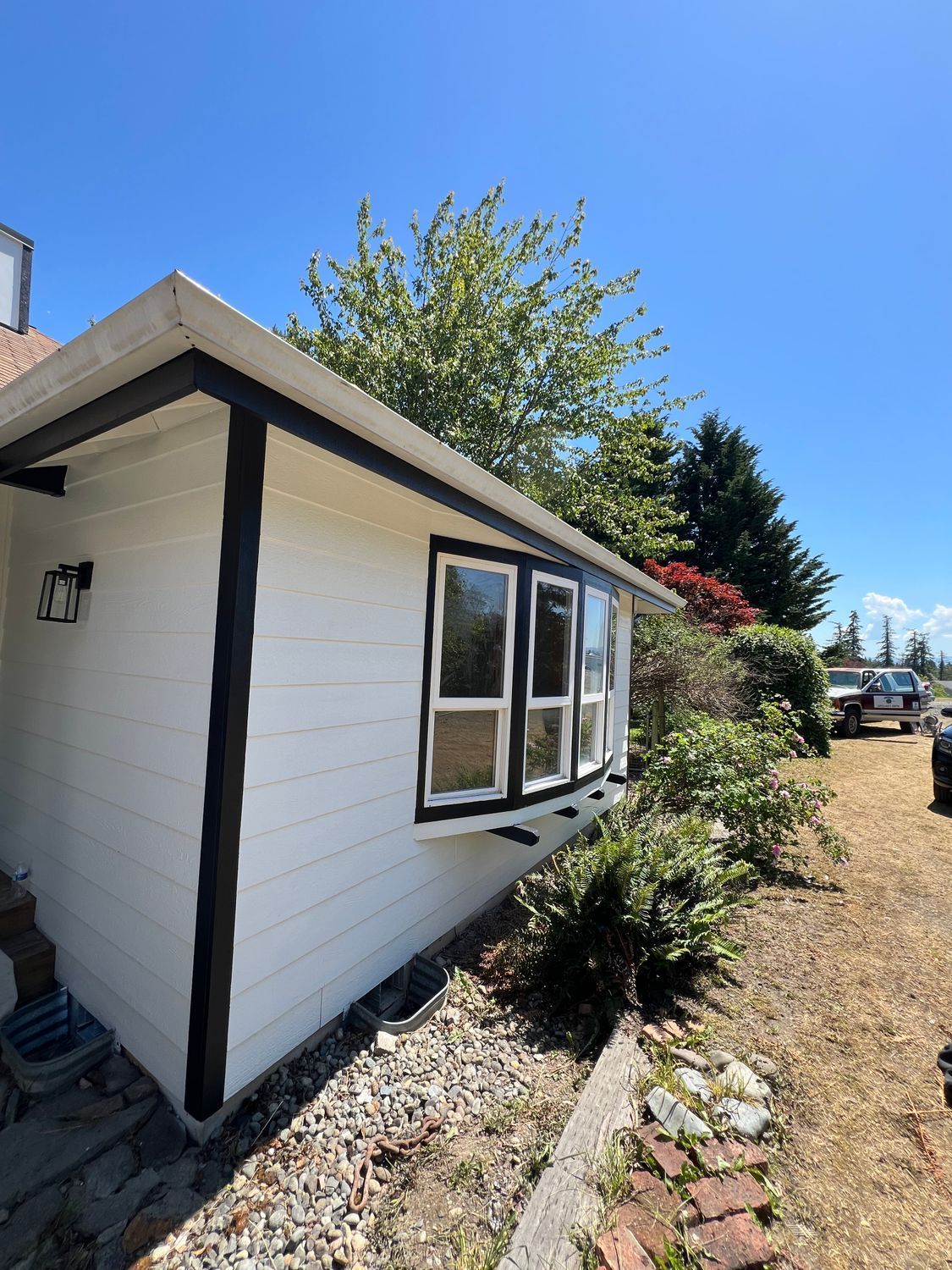 White house exterior with black trim, bay window, and greenery on a sunny day.