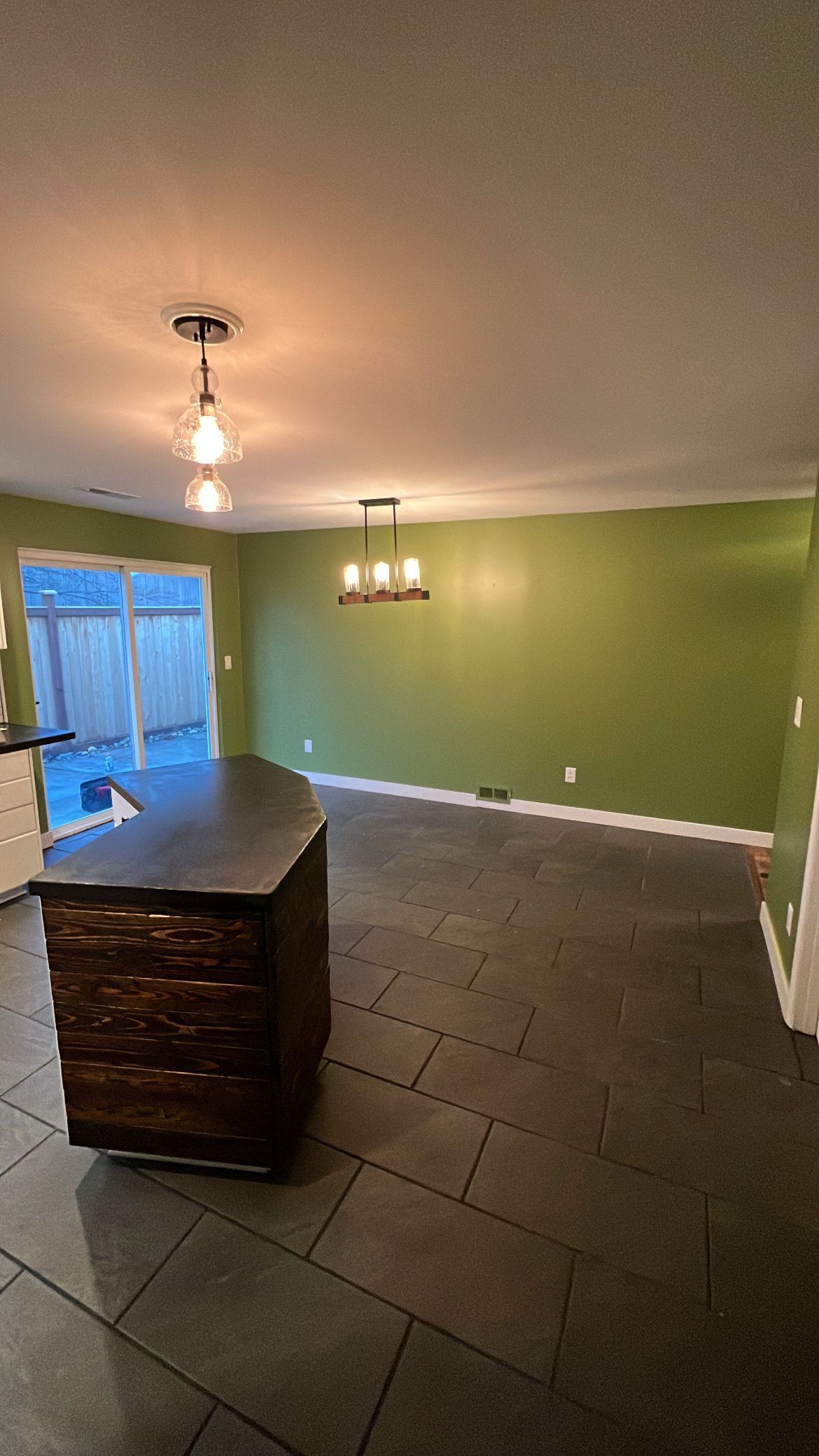 Kitchen with island, dark floor, green wall, sliding door, and pendant lights.