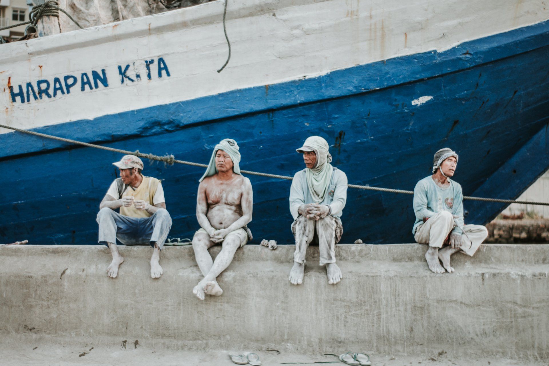 A group of people are sitting on a wall in front of a boat.