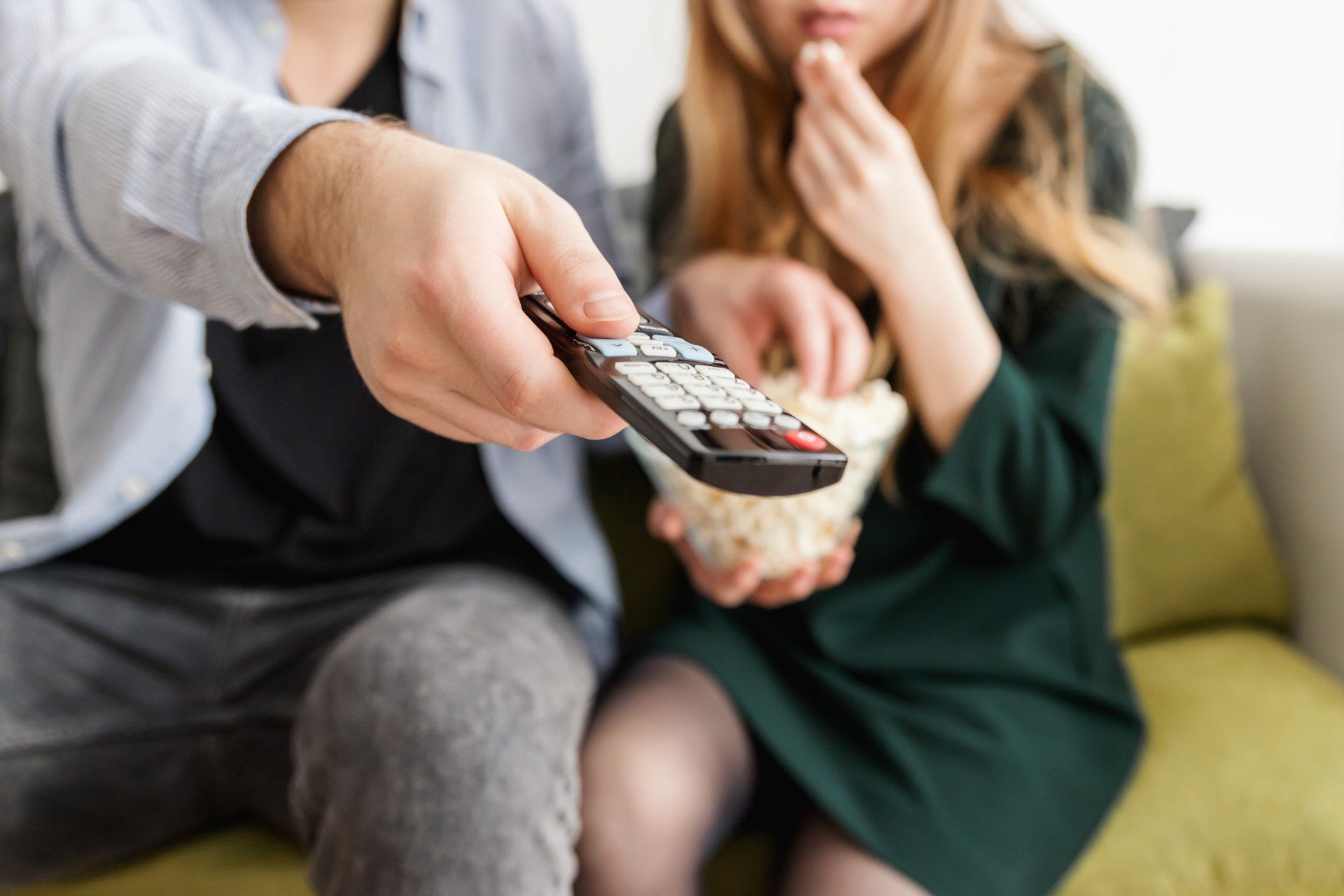 Photo by JESHOOTS.com A man is holding a remote control while a woman eats popcorn.