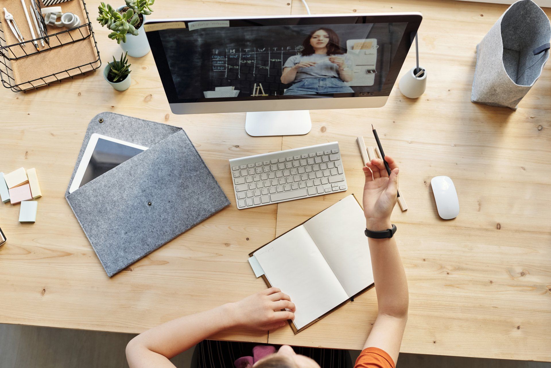 A person is sitting at a desk with a computer and a notebook.