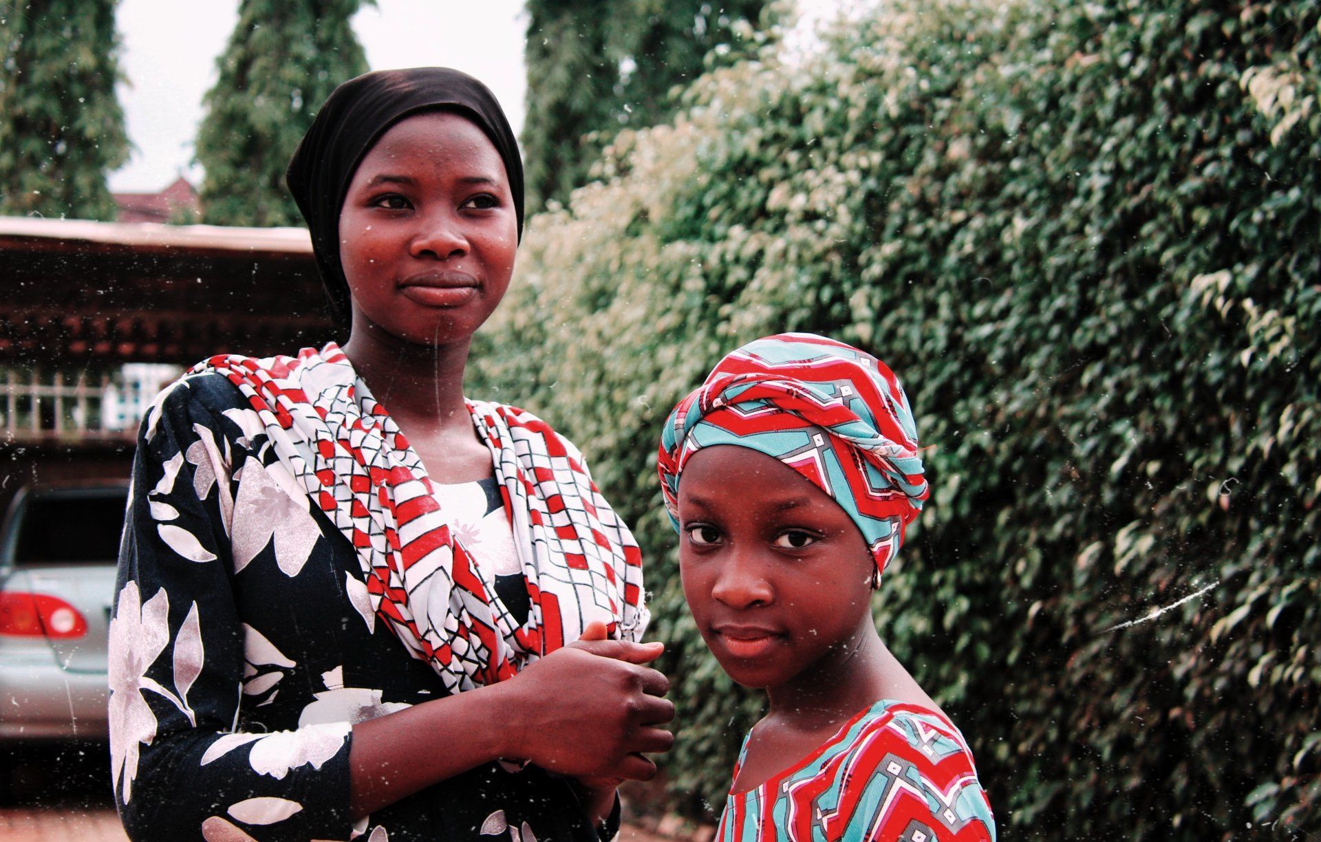 A woman and a little girl are standing next to each other in front of a bush.