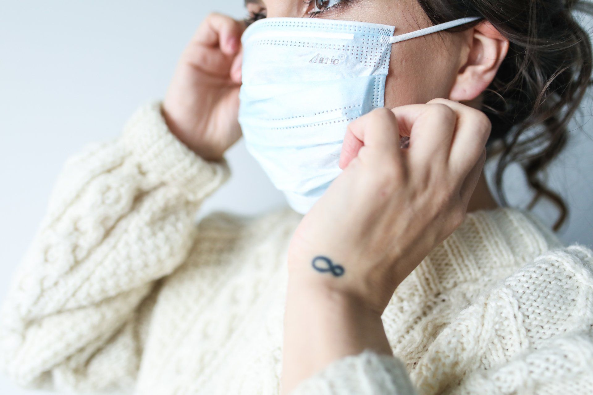 A woman wearing a face mask with an infinity tattoo on her wrist.