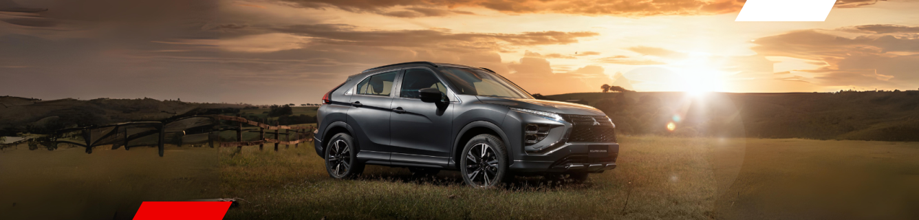 Um SUV Mitsubishi Eclipse Cross cinza escuro estacionado em um campo gramado com o pôr do sol ao fundo.
