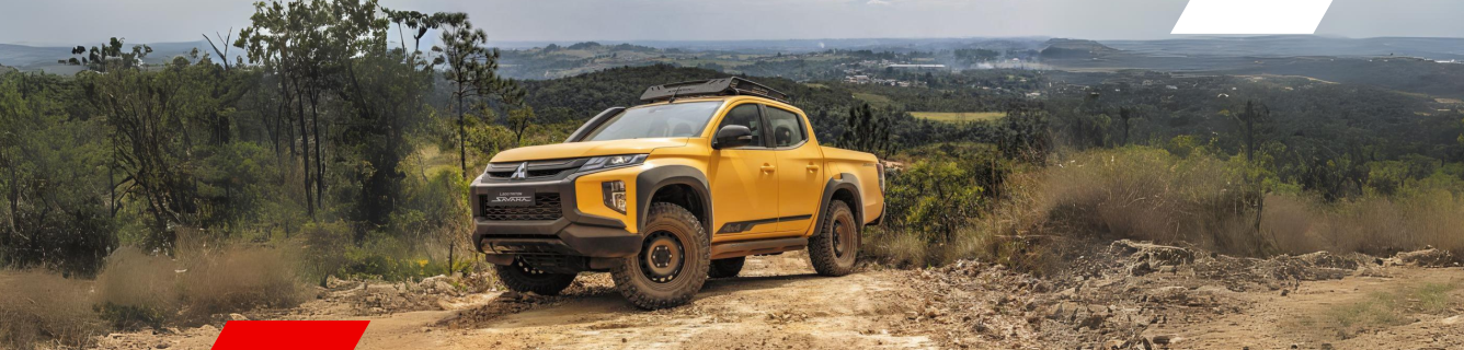 Caminhonete amarela trafegando por uma estrada de terra em uma paisagem verdejante e montanhosa.