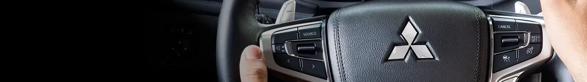 Volante com o logotipo da Mitsubishi. Uma mão é visível.