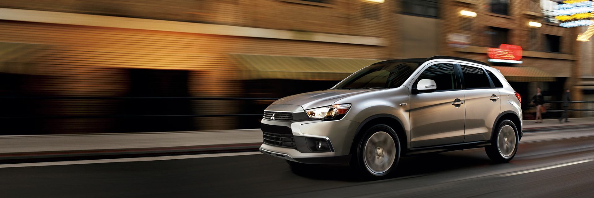 SUV prateado trafegando em uma rua da cidade à noite, com efeito de desfoque de movimento.