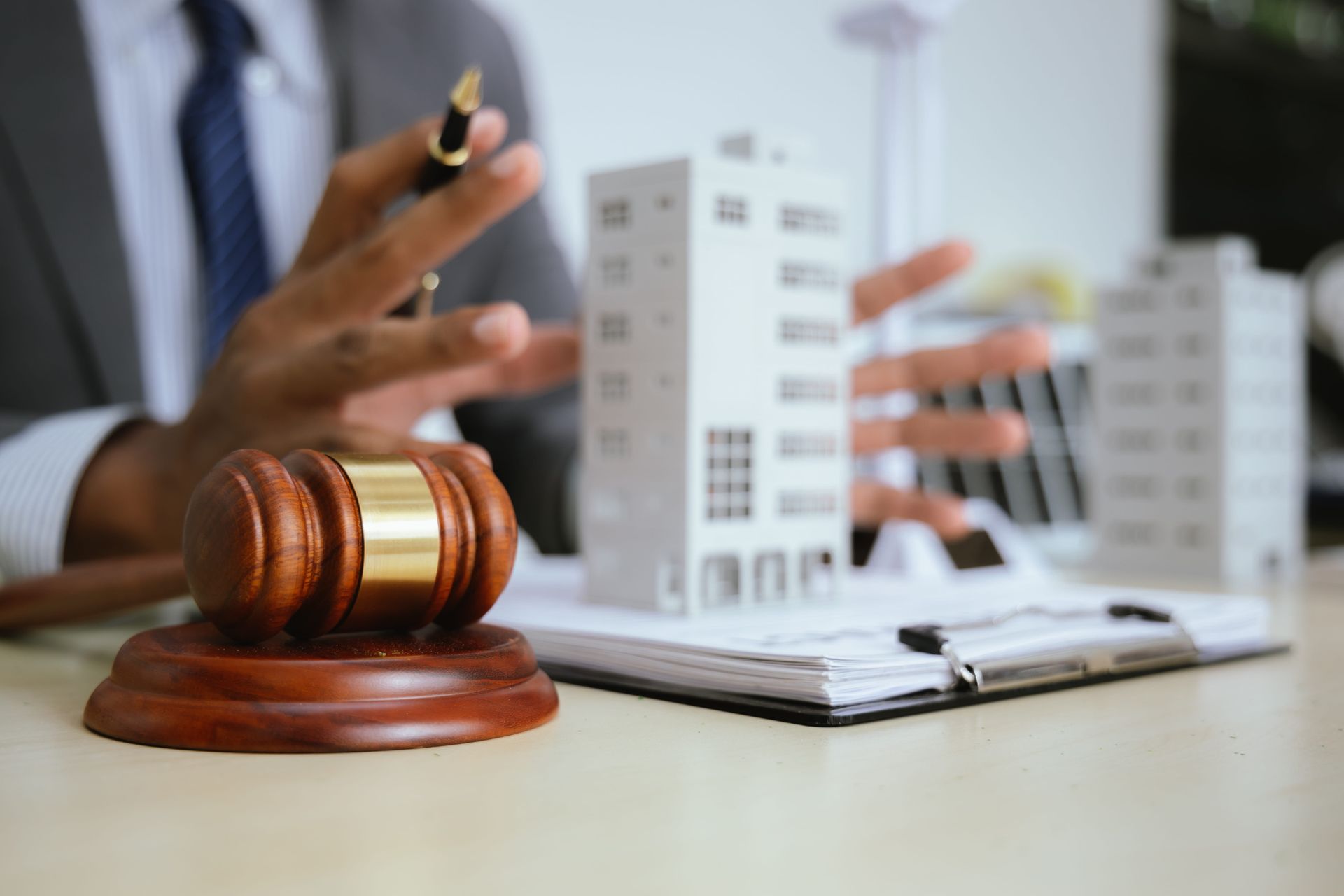 Gavel on table with model buildings, person in suit gesturing; legal or real estate context.
