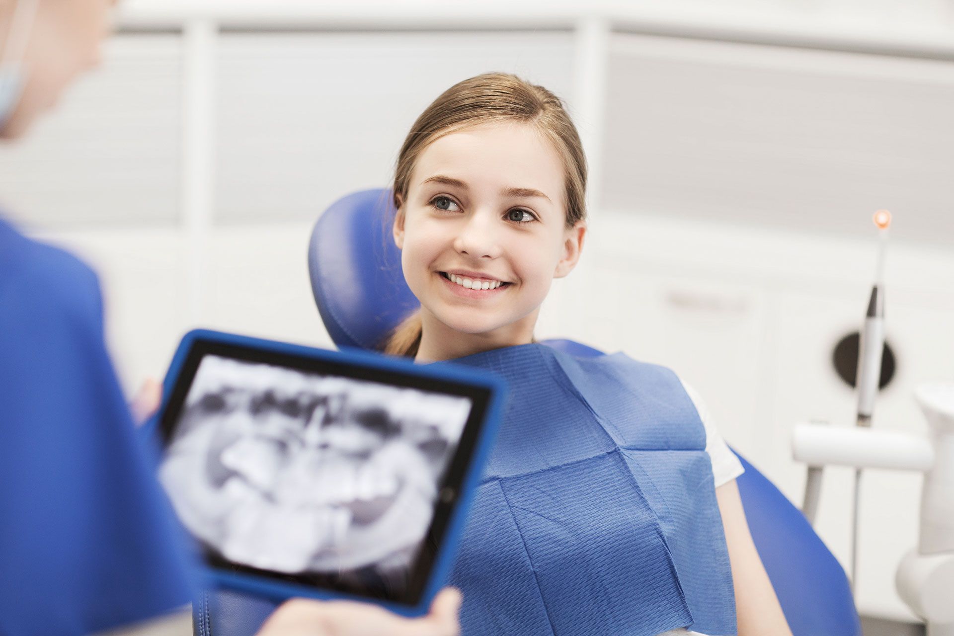 Dentist showing a smiling teen patient an X-ray on a tablet in a bright dental office.