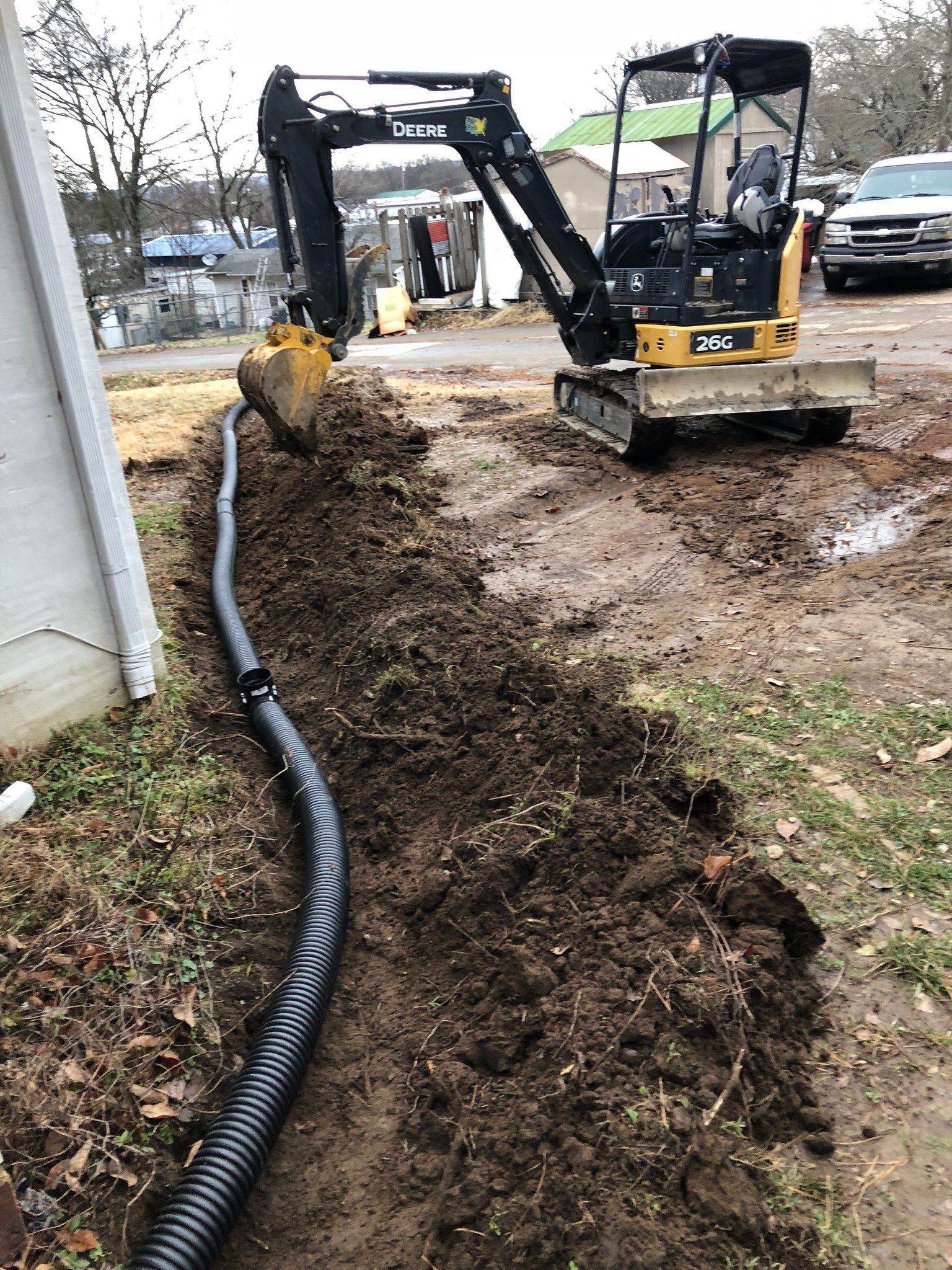 A small excavator is digging a hole in the ground next to a house.
