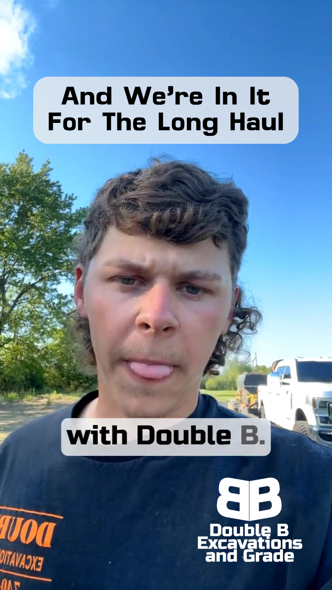 A man with his tongue out is wearing a double b excavations and grade shirt.