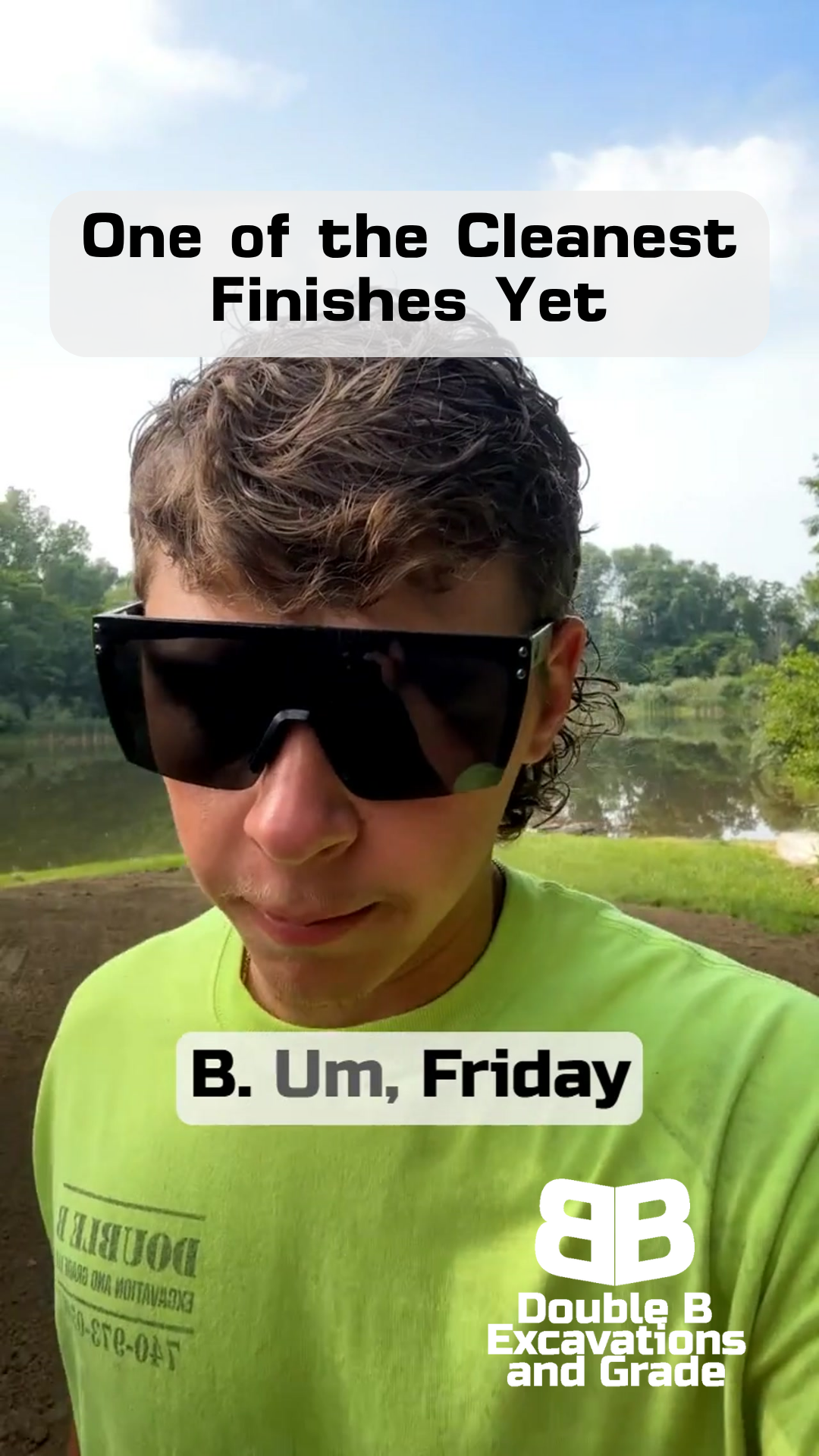 A man wearing sunglasses and a green shirt is standing in front of a lake.