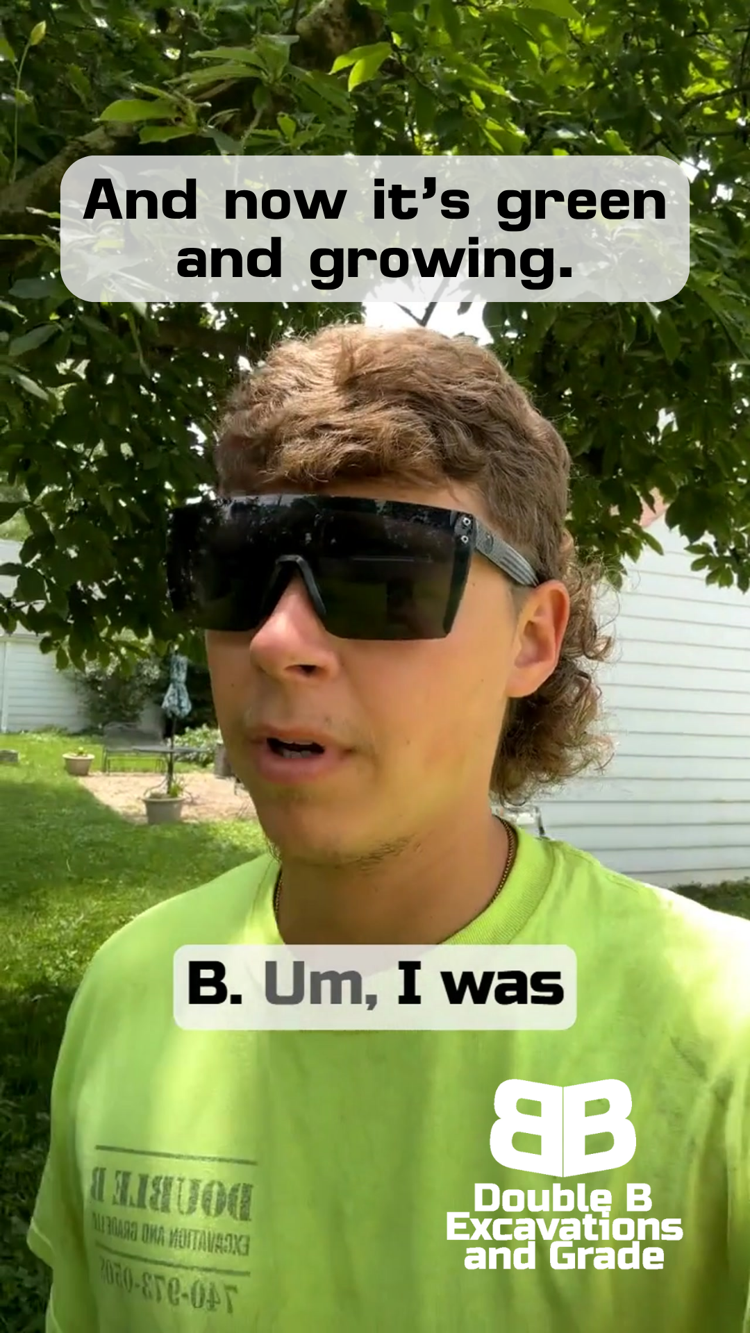 A man wearing sunglasses and a green shirt is standing in front of a tree.