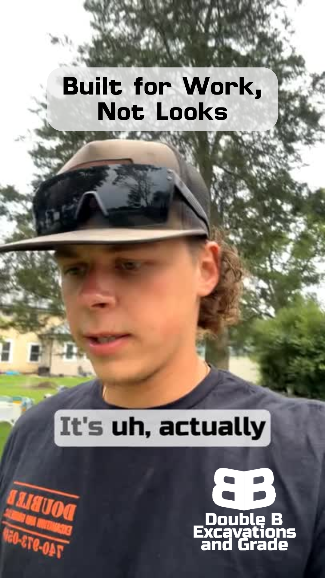 A man wearing a hat and sunglasses is standing in front of a tree.
