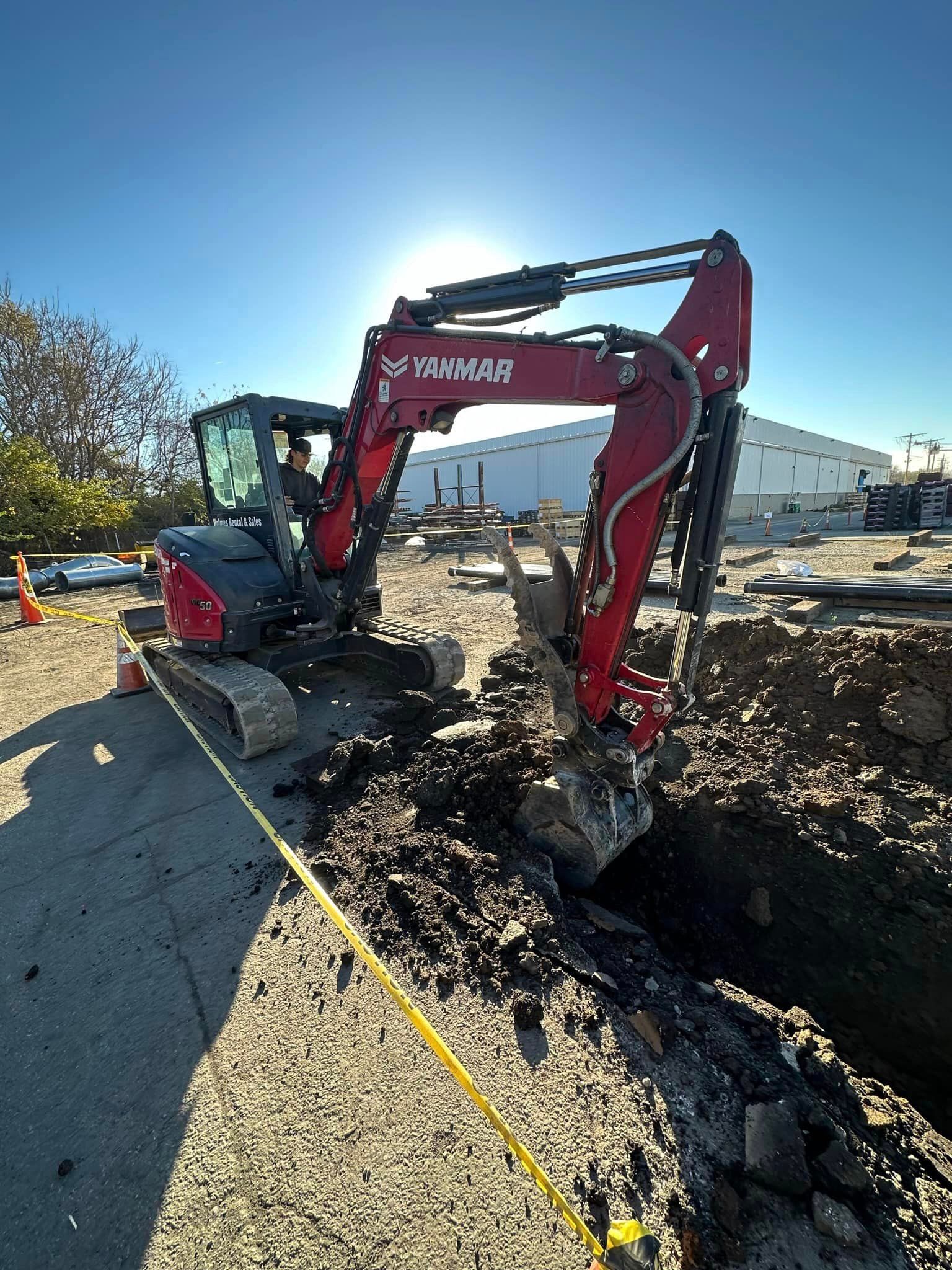 A red excavator is digging a hole in the dirt on a construction site.