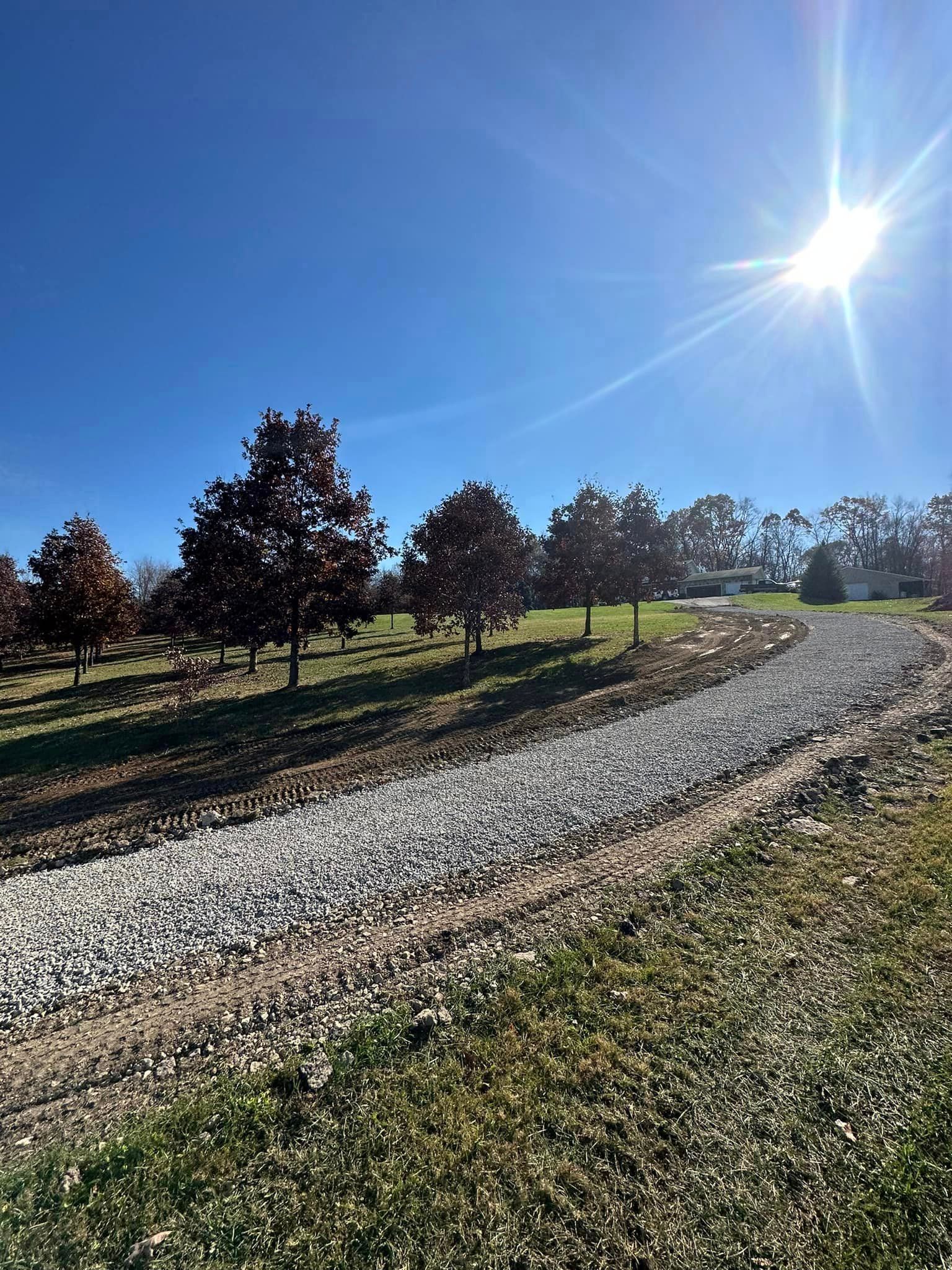 A gravel road going through a grassy field with trees on both sides.