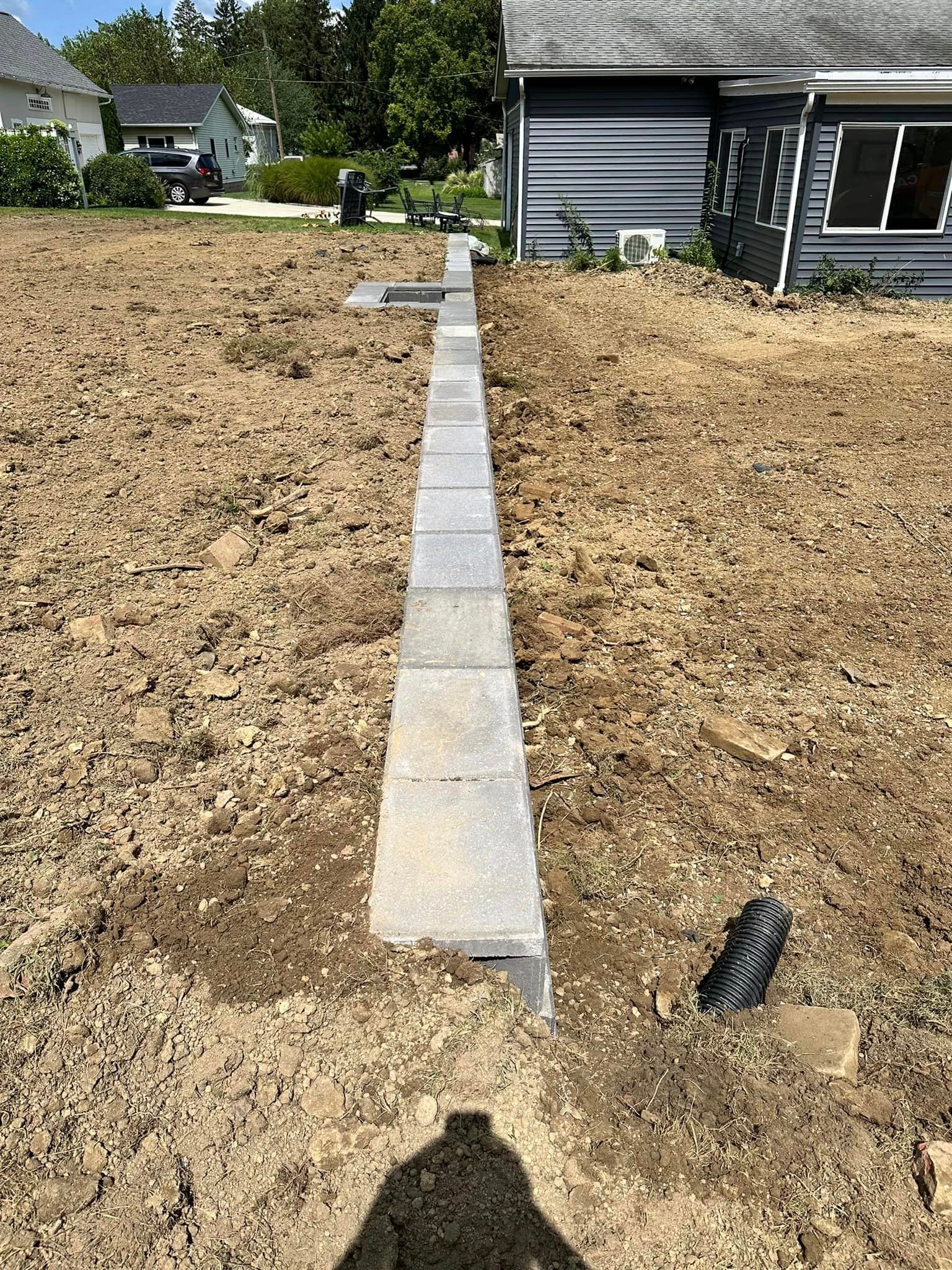 A concrete walkway is being built in a dirt field in front of a house.