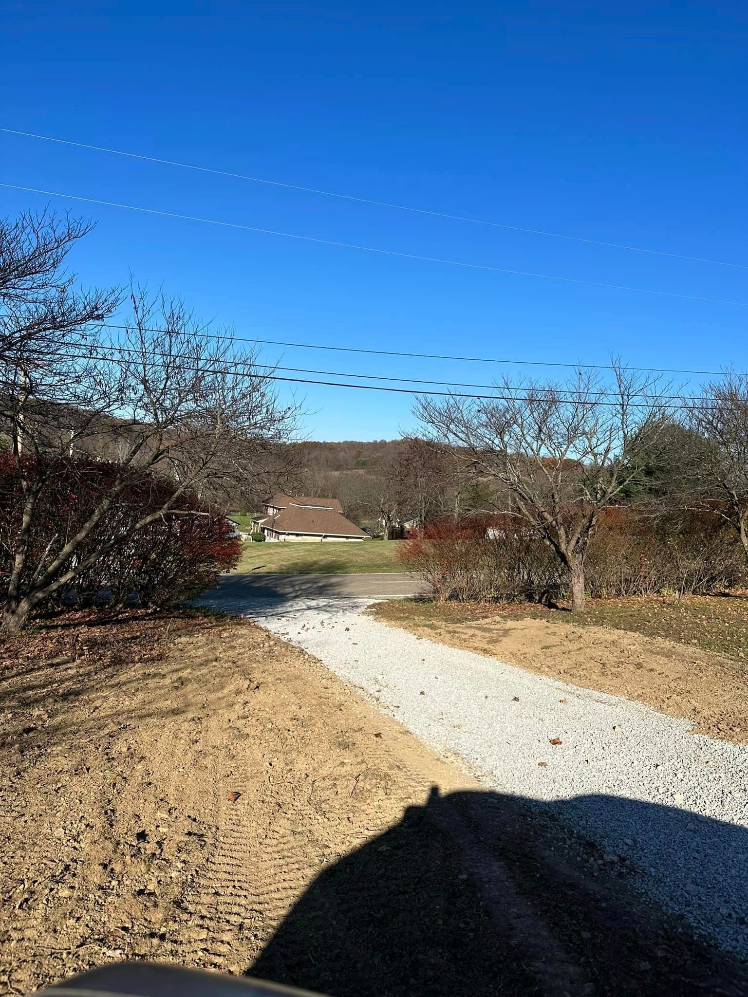 A flock of geese are flying over a dirt road.