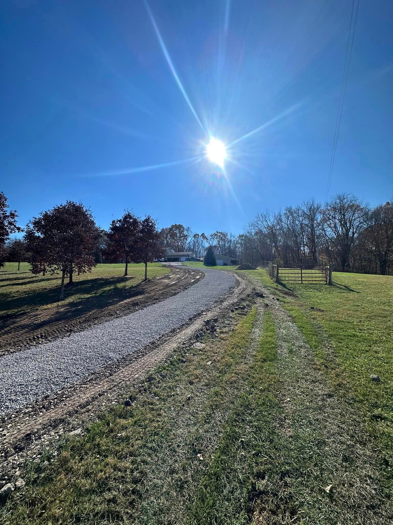 The sun is shining brightly over a dirt road in a field.