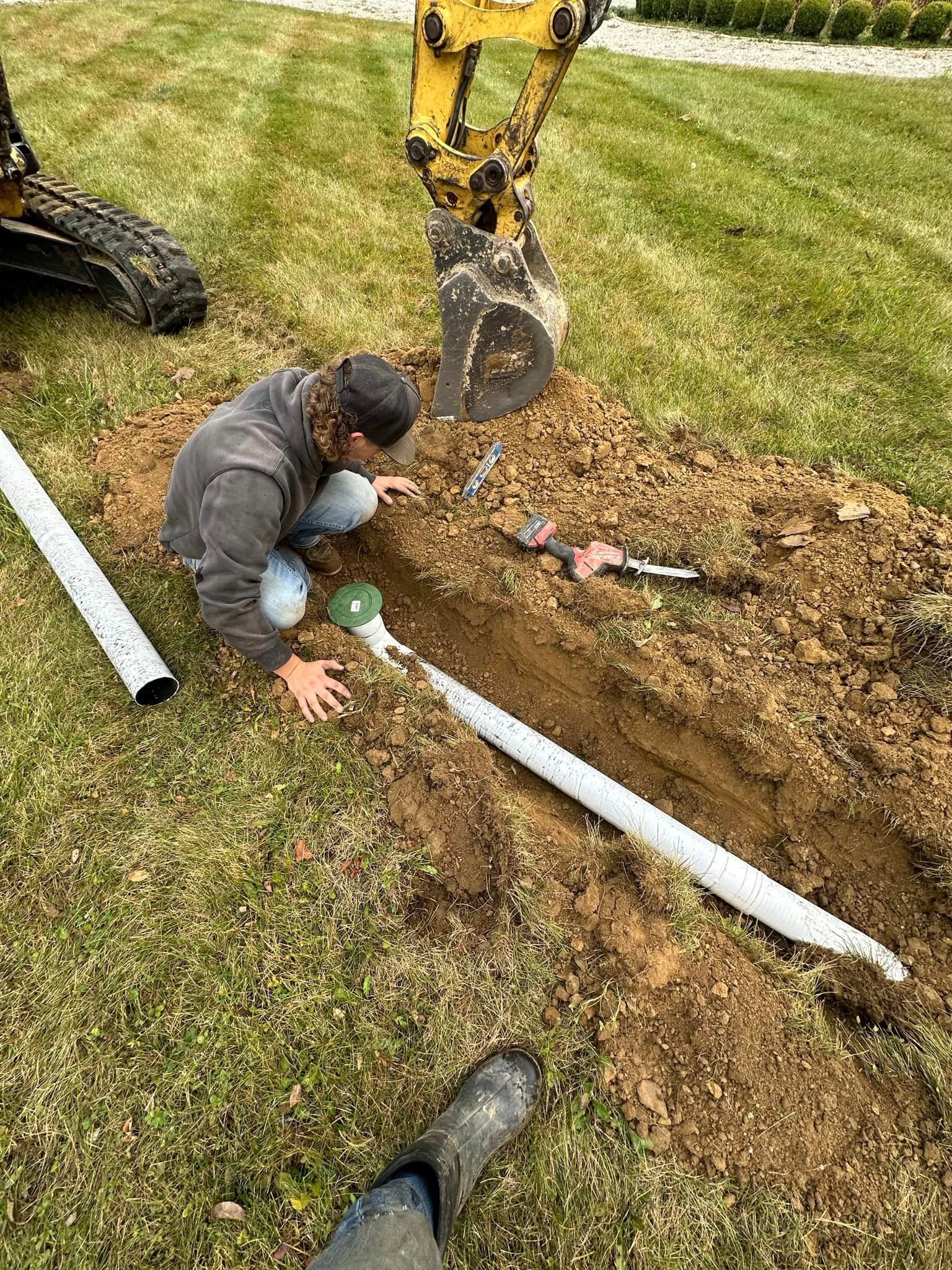 A man is kneeling in the dirt working on a pipe.