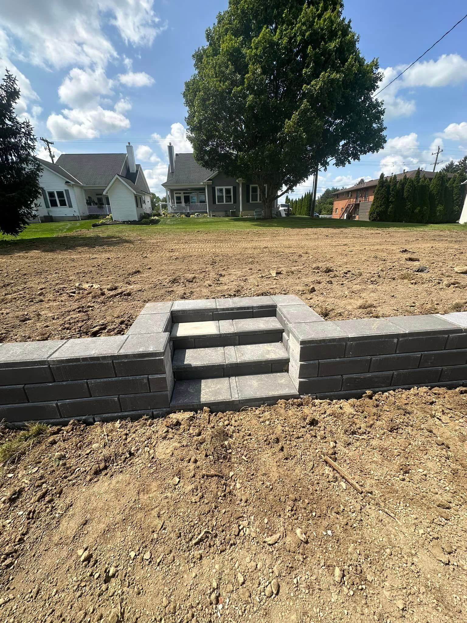 A brick wall with stairs leading up to a house in the background.