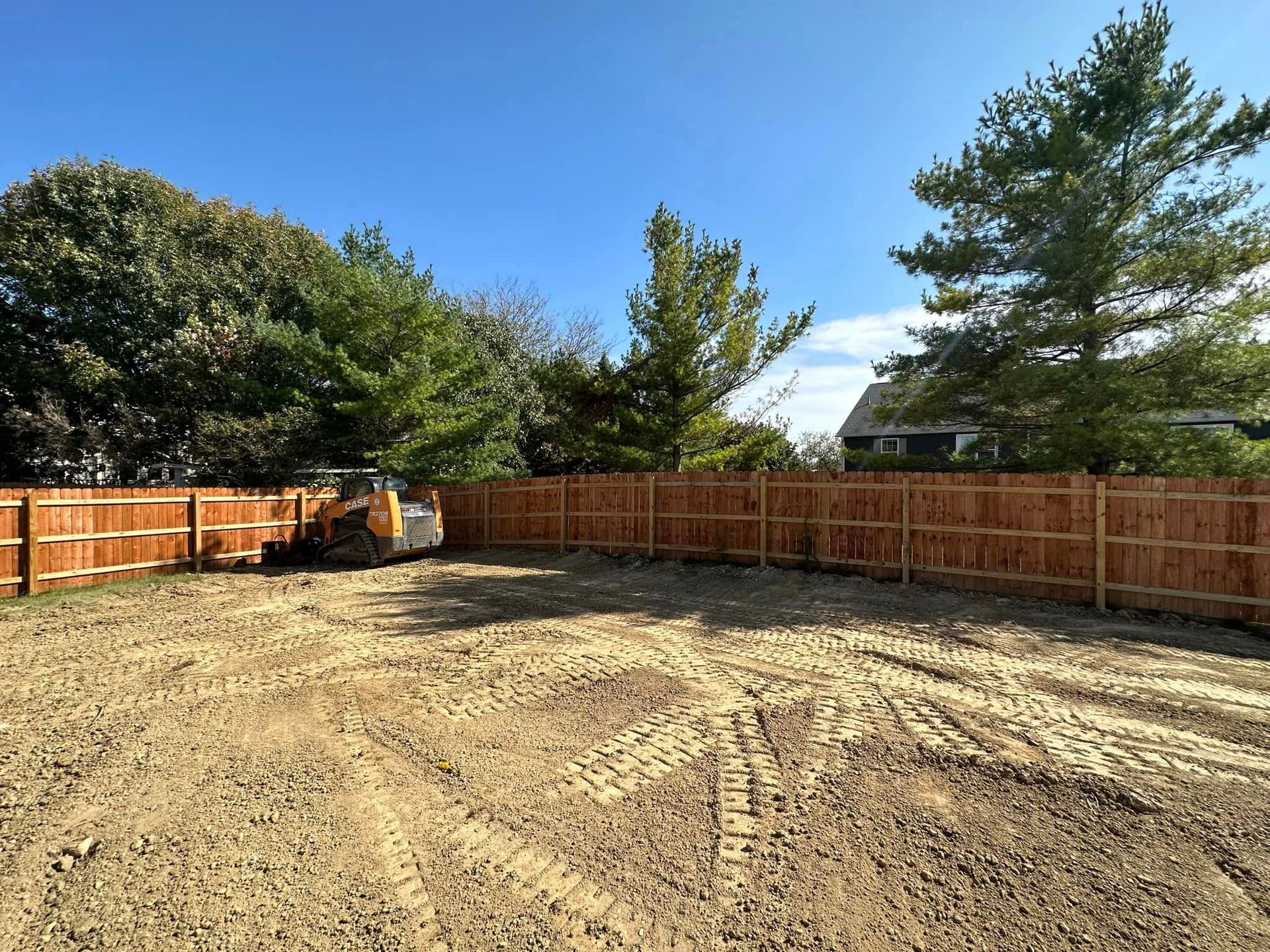 A backyard with a wooden fence and a bulldozer in the dirt.