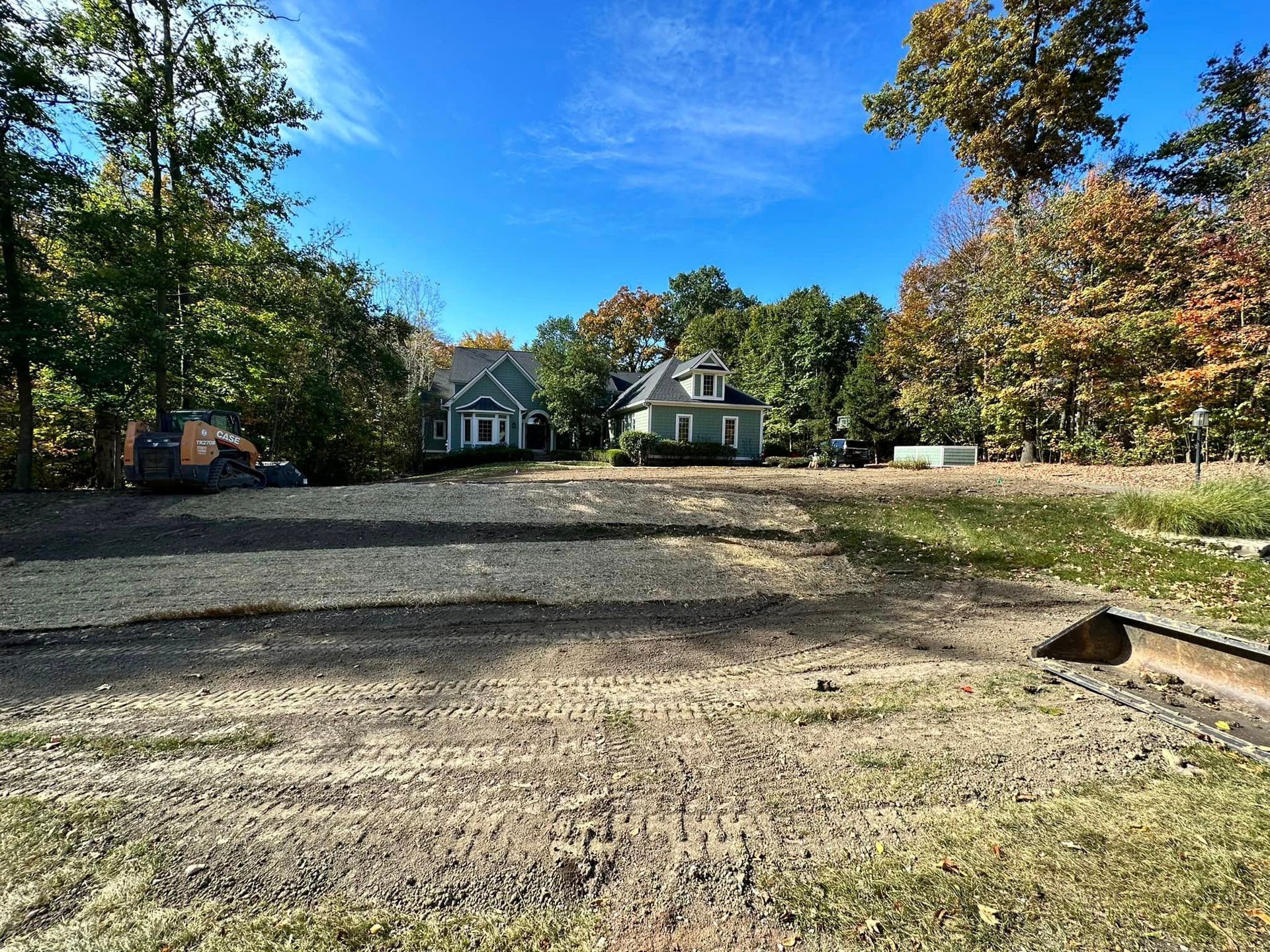 A dirt road leading to a house surrounded by trees on a sunny day.