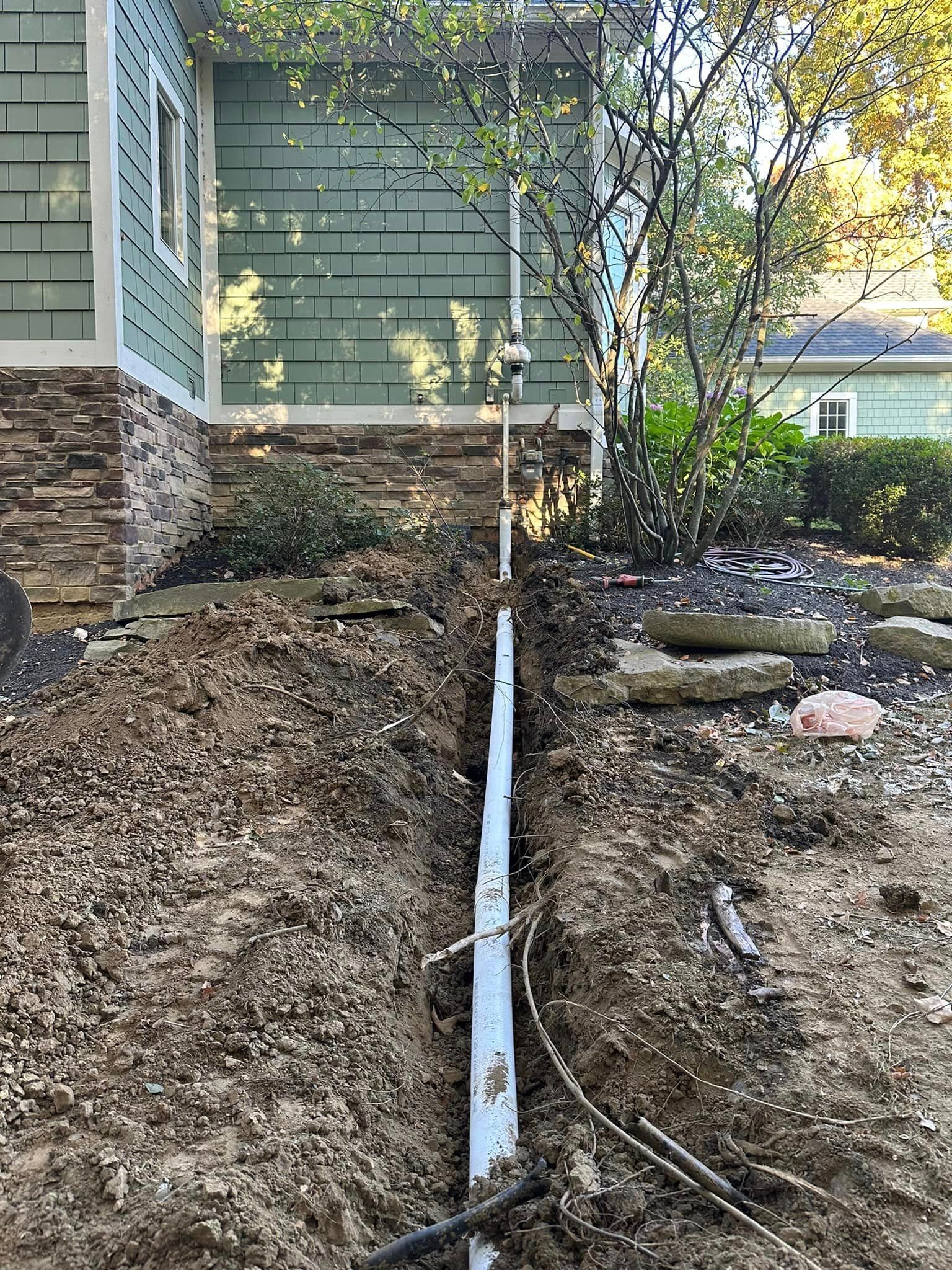 A pipe is being installed in the dirt in front of a house.