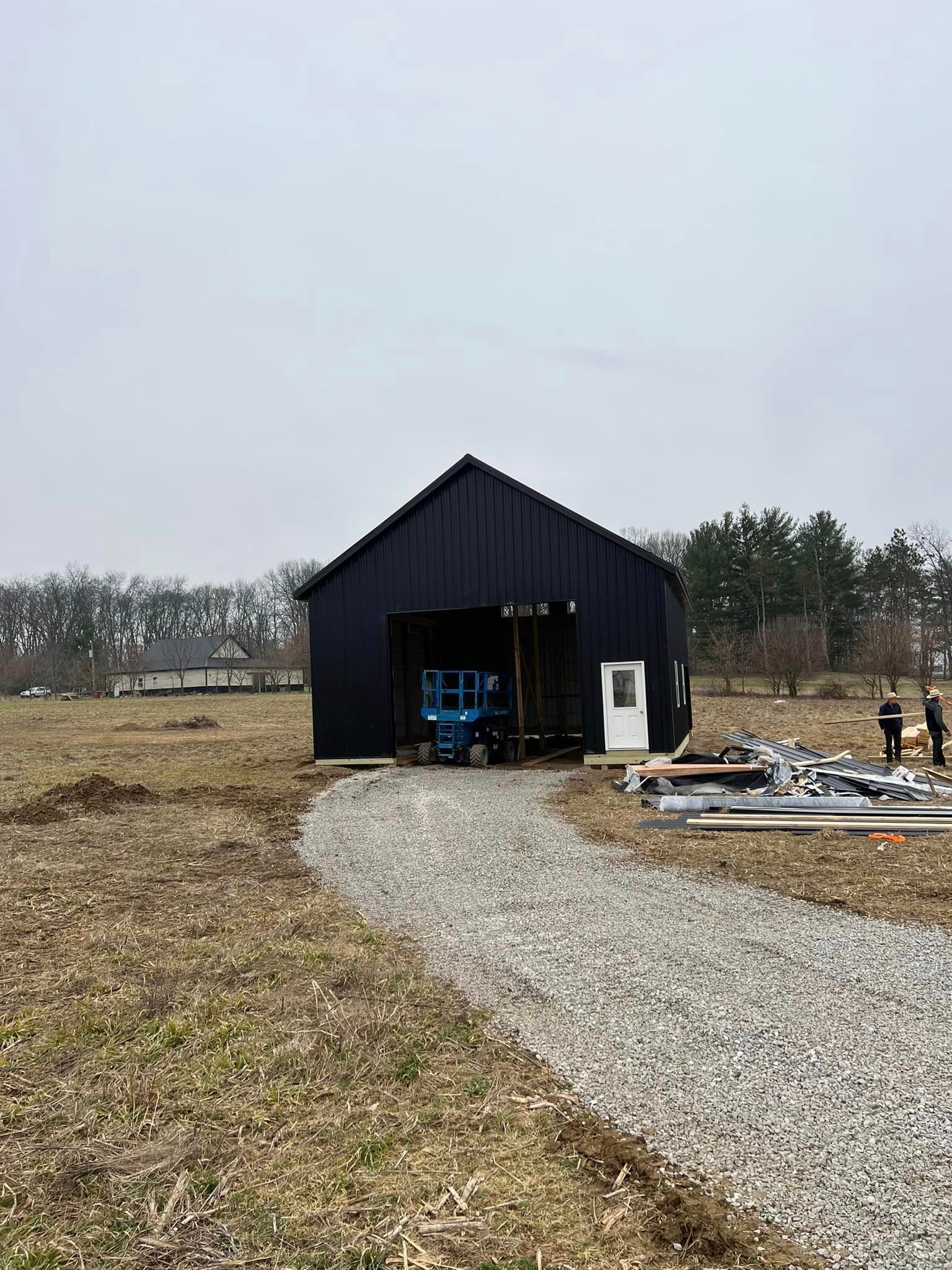 A black barn is being built in the middle of a field.