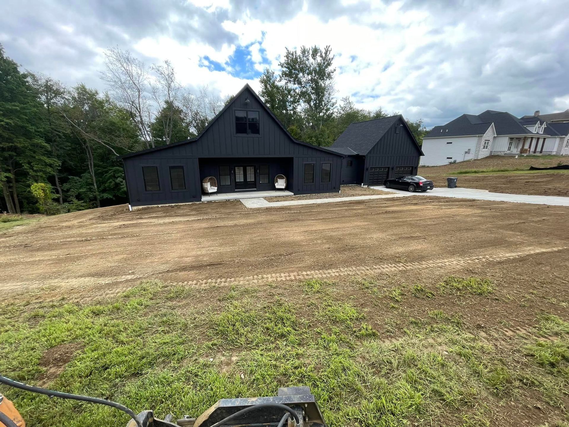 A lawn mower is cutting grass in front of a black house.