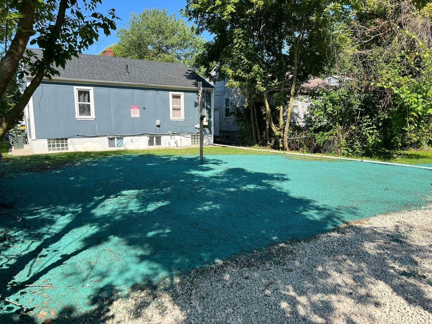 A blue house with a green basketball court in front of it.