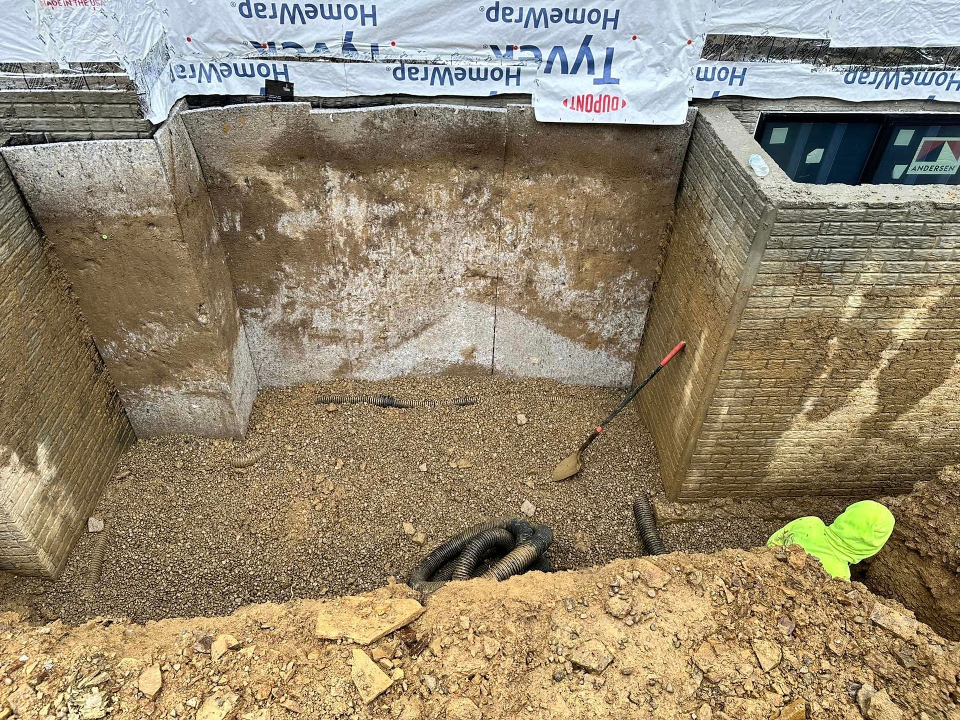 A man is digging a hole in the ground next to a brick wall.