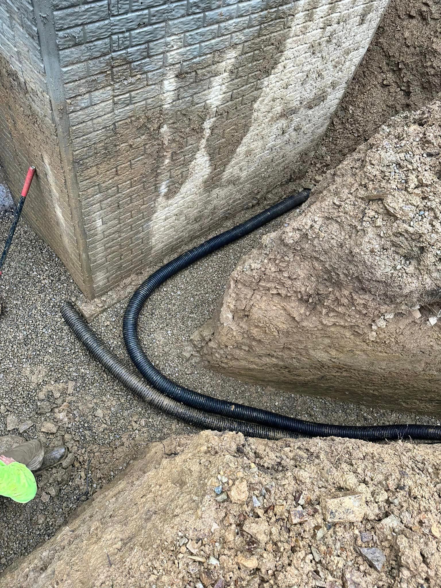 A black hose is laying in the dirt next to a brick wall.