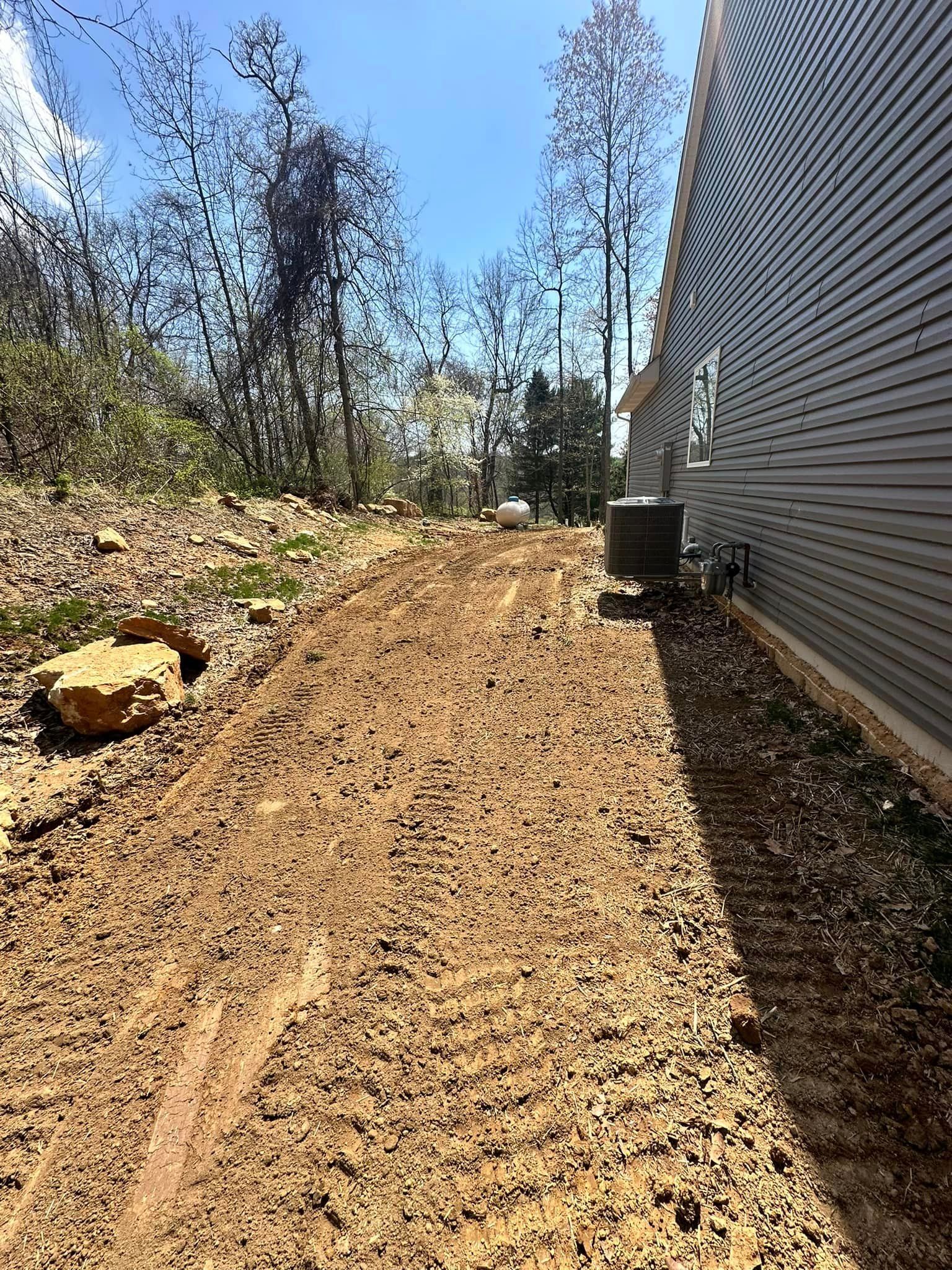 A dirt road leading to a house with trees in the background.