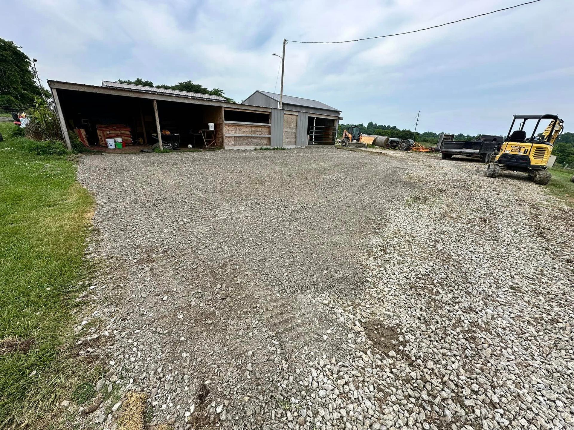 A gravel road leading to a building with a yellow excavator in the background.