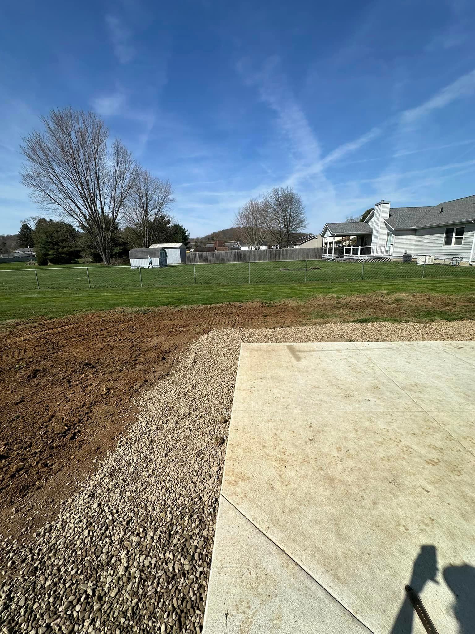 A concrete driveway leading to a grassy field with a house in the background.