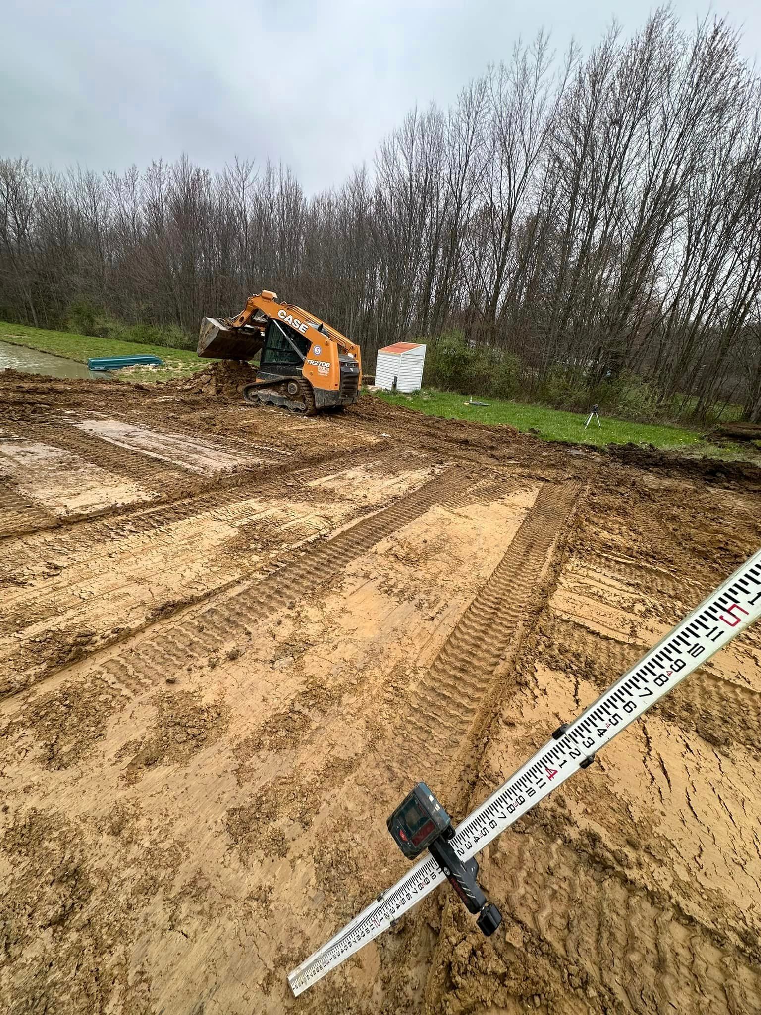 A measuring stick is sitting on top of a dirt field next to a bulldozer.