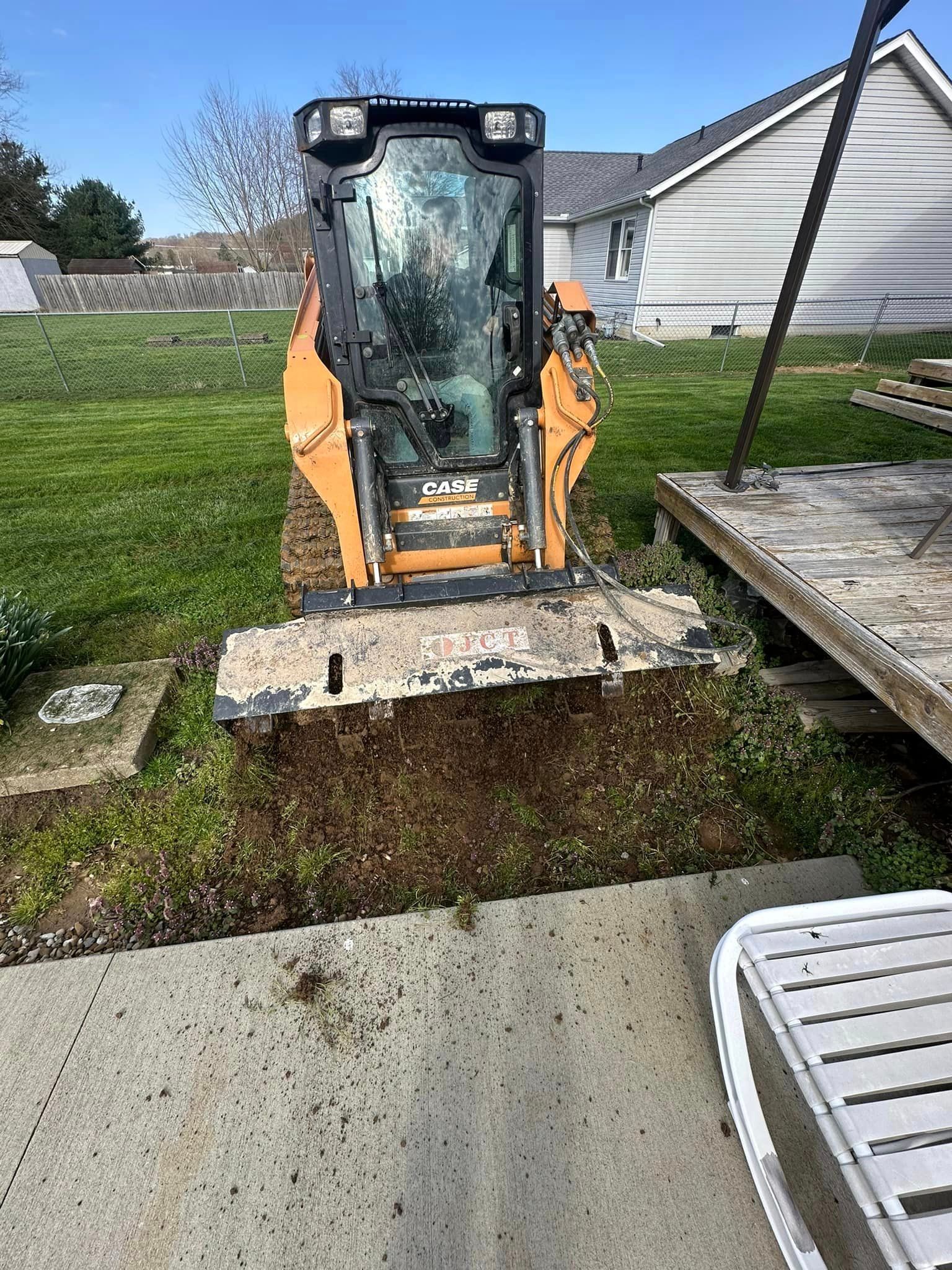 A small bulldozer is digging a hole in the ground in a backyard.