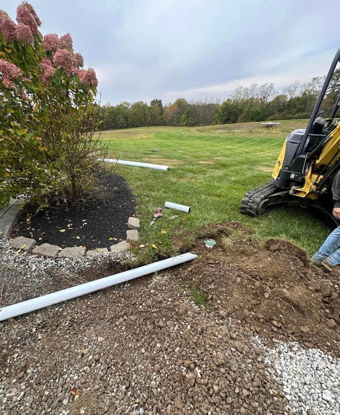 A man is digging a hole in the ground next to a yellow excavator.