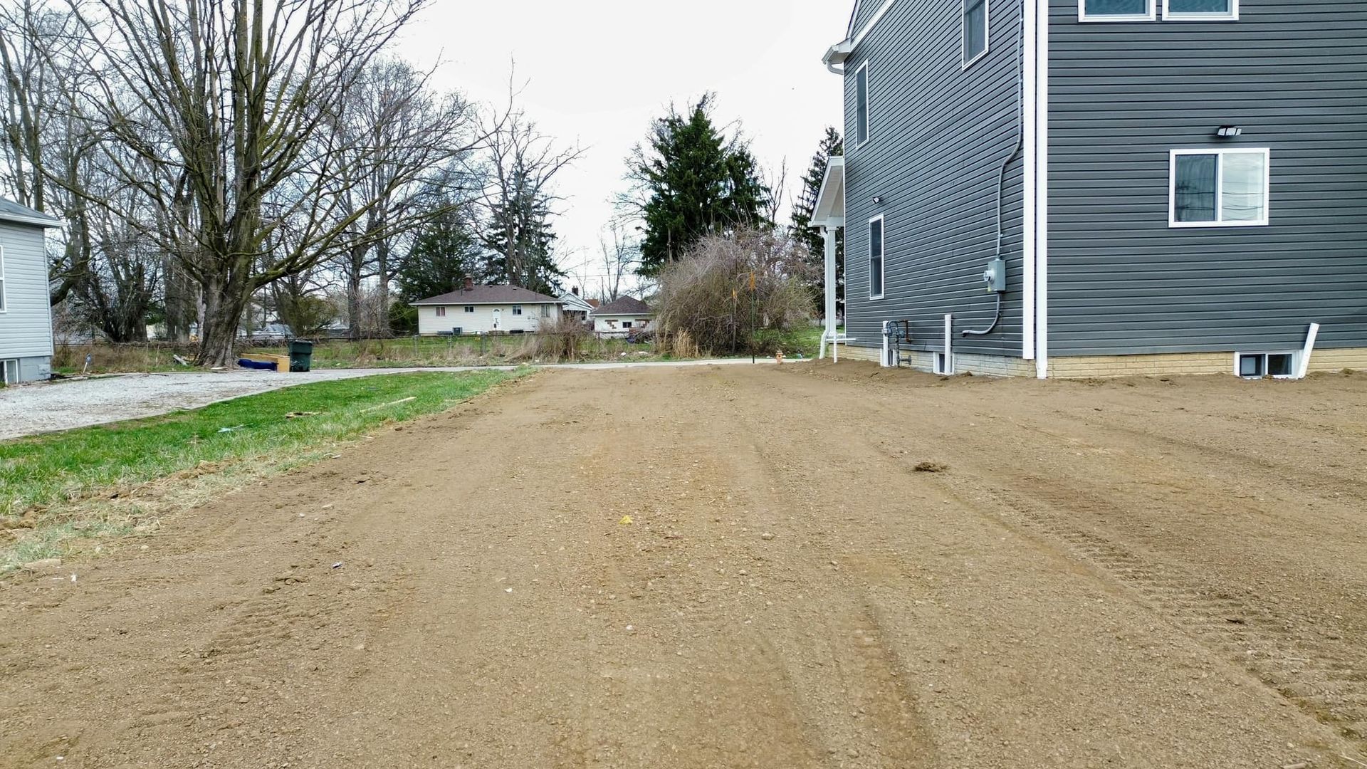 A dirt road leading to a house with trees in the background.