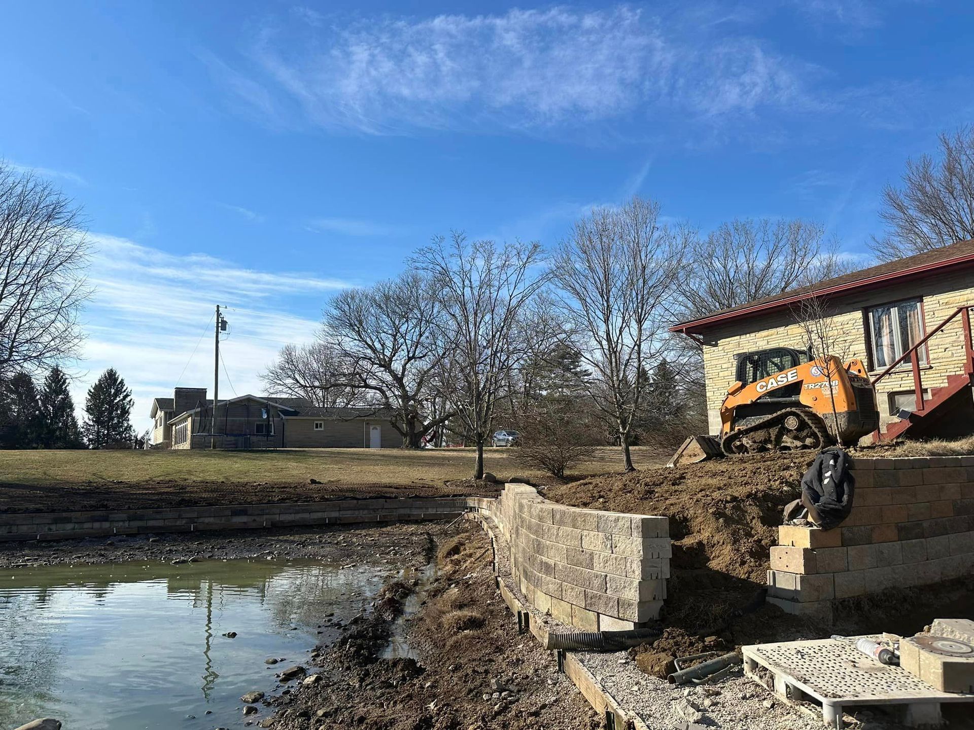 A house is being built next to a pond with a bulldozer in the background.