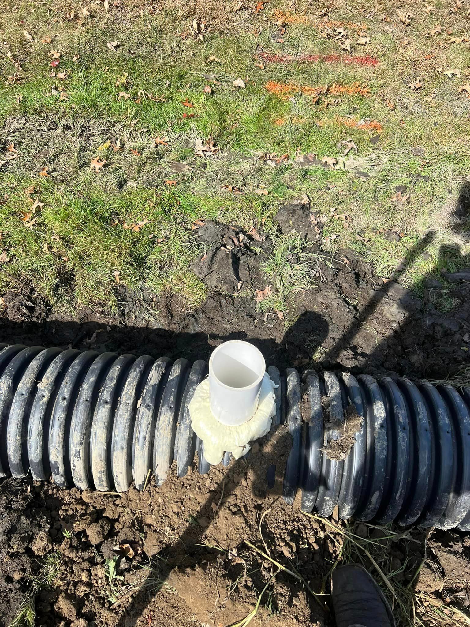 A drain pipe is sitting in the dirt next to a grassy field.