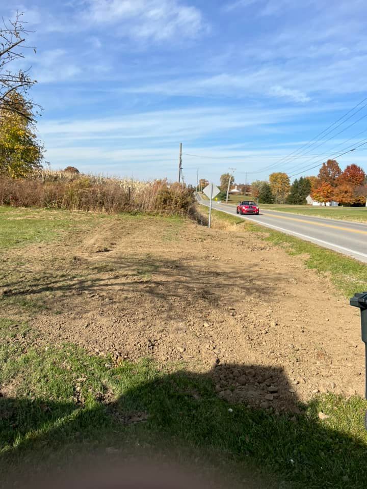 A red car is driving down a dirt road next to a field.