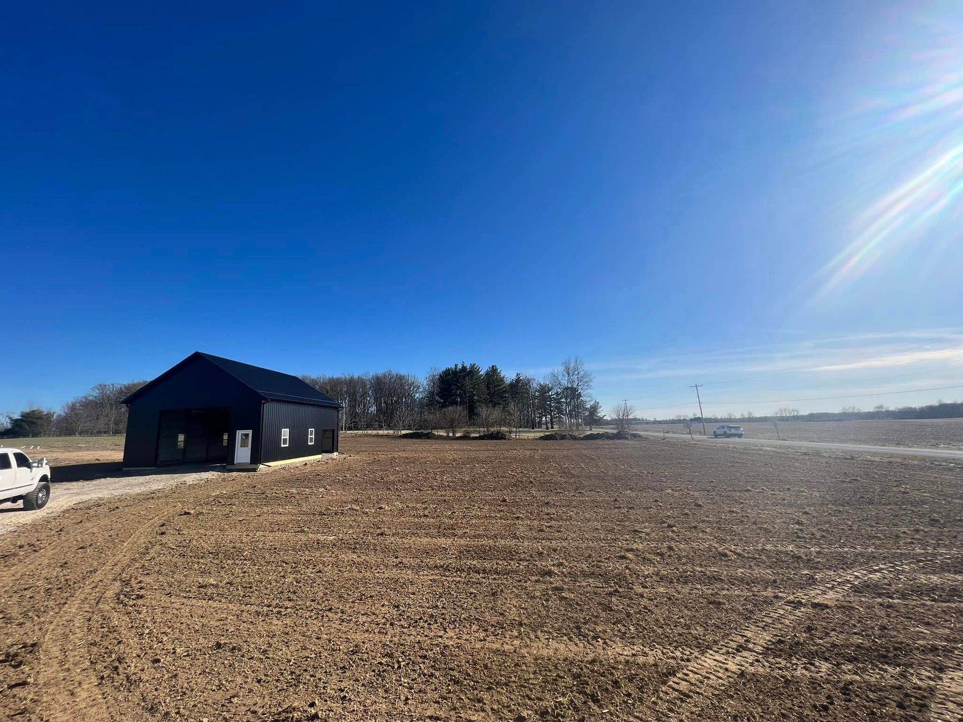 A white truck is parked in front of a barn in a field.