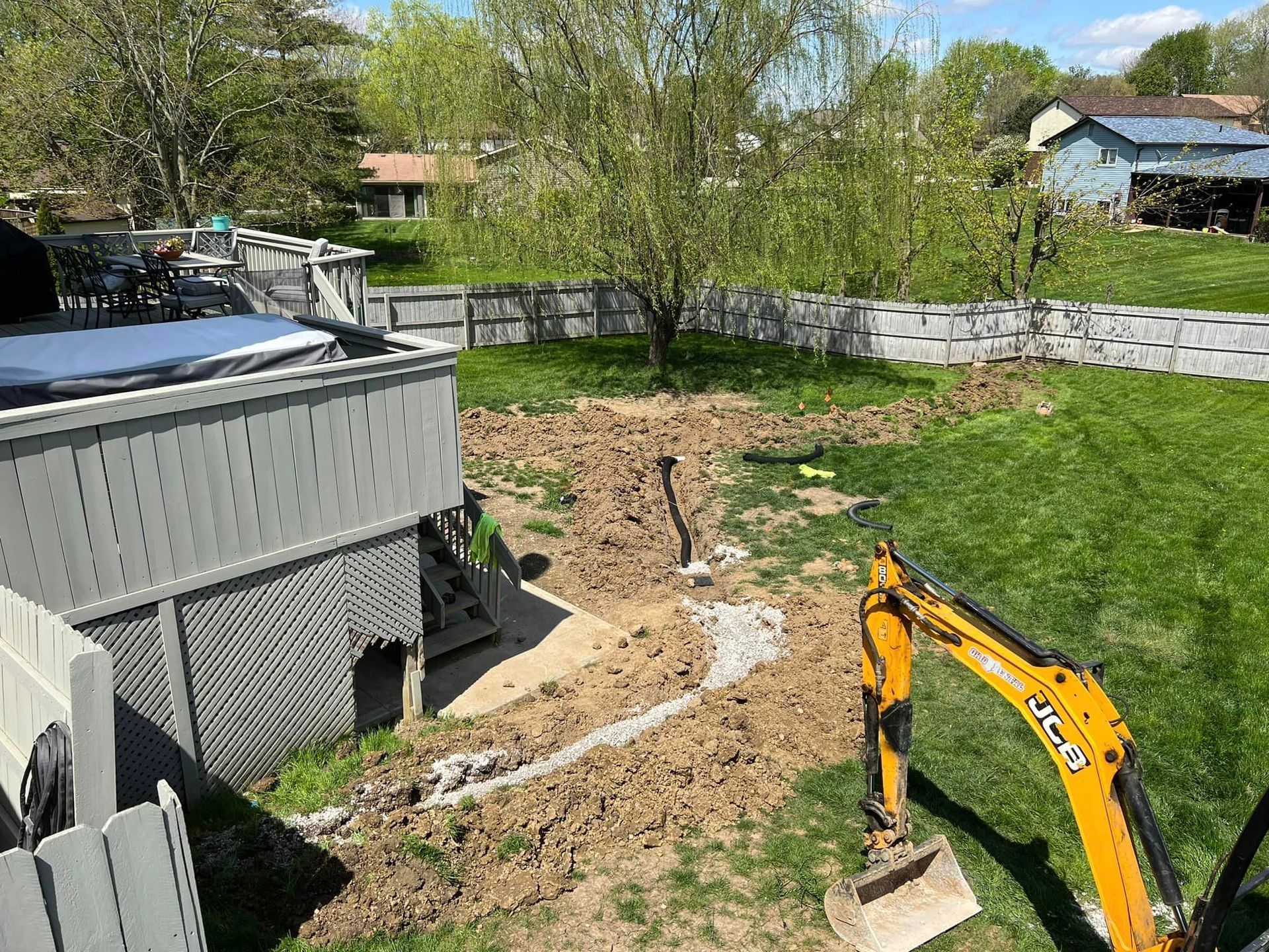 A yellow excavator is digging a hole in a yard in front of a house.