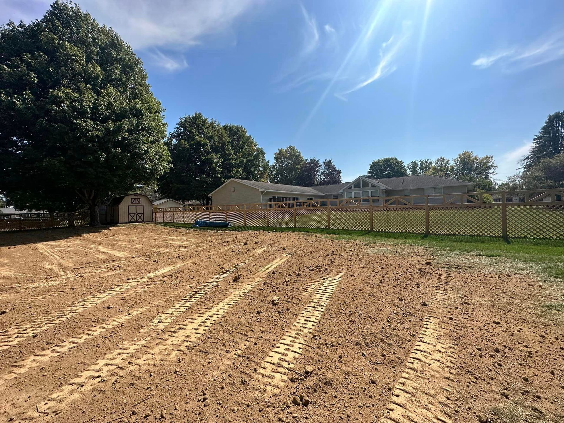 A dirt field with a fence and a house in the background