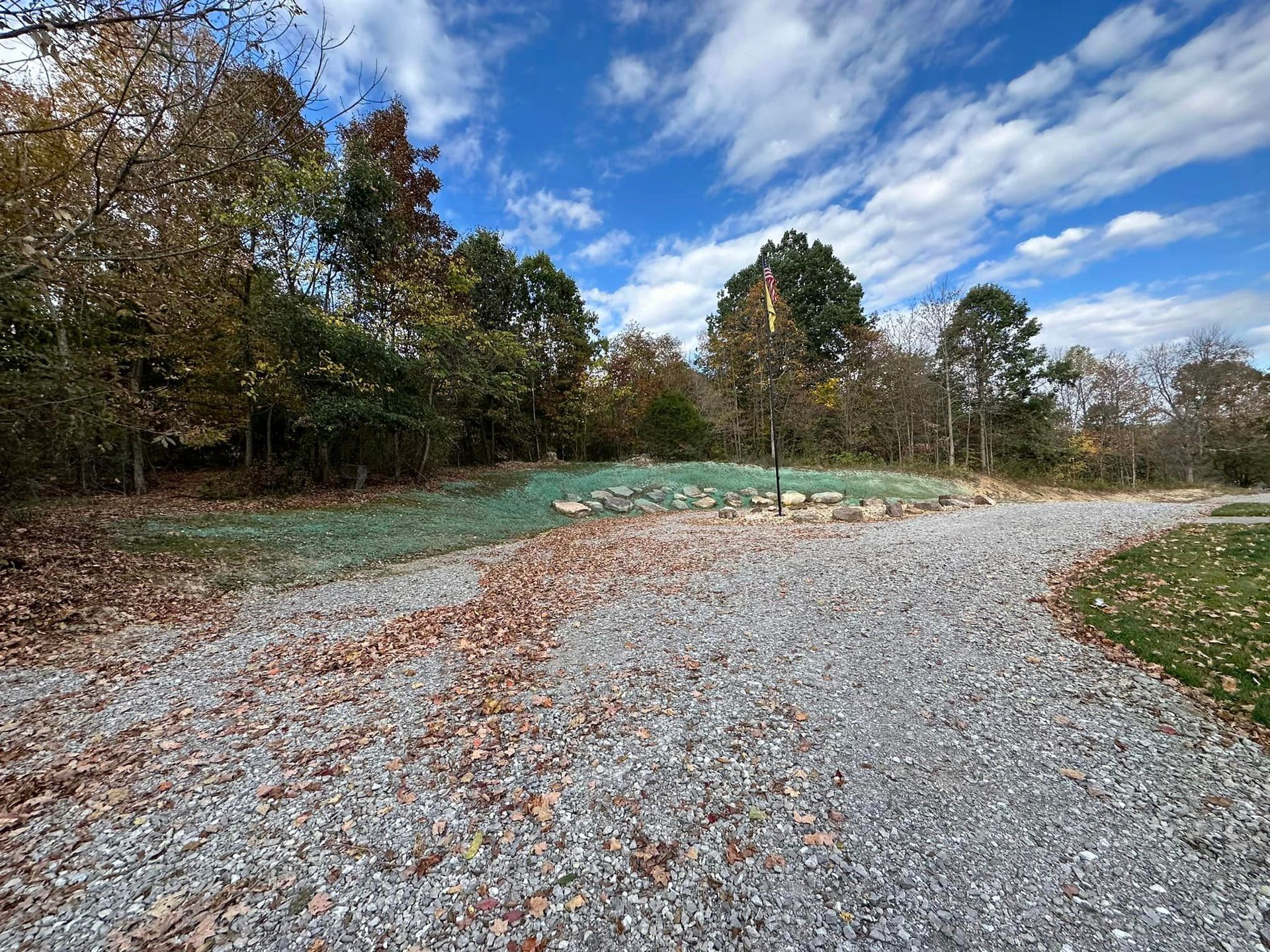 A gravel road leading to a green field with trees in the background.