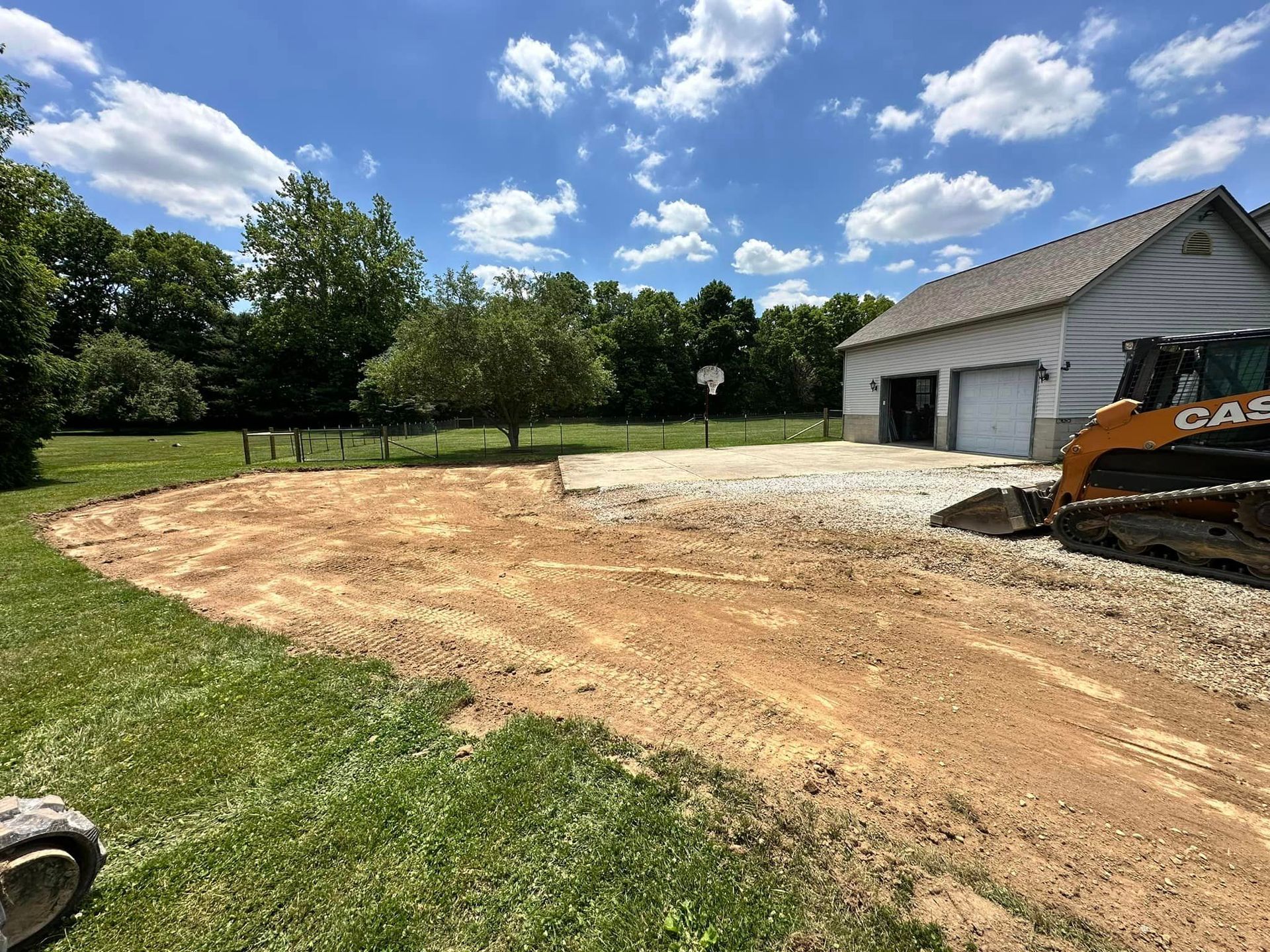 A bulldozer is driving down a dirt road in front of a garage.